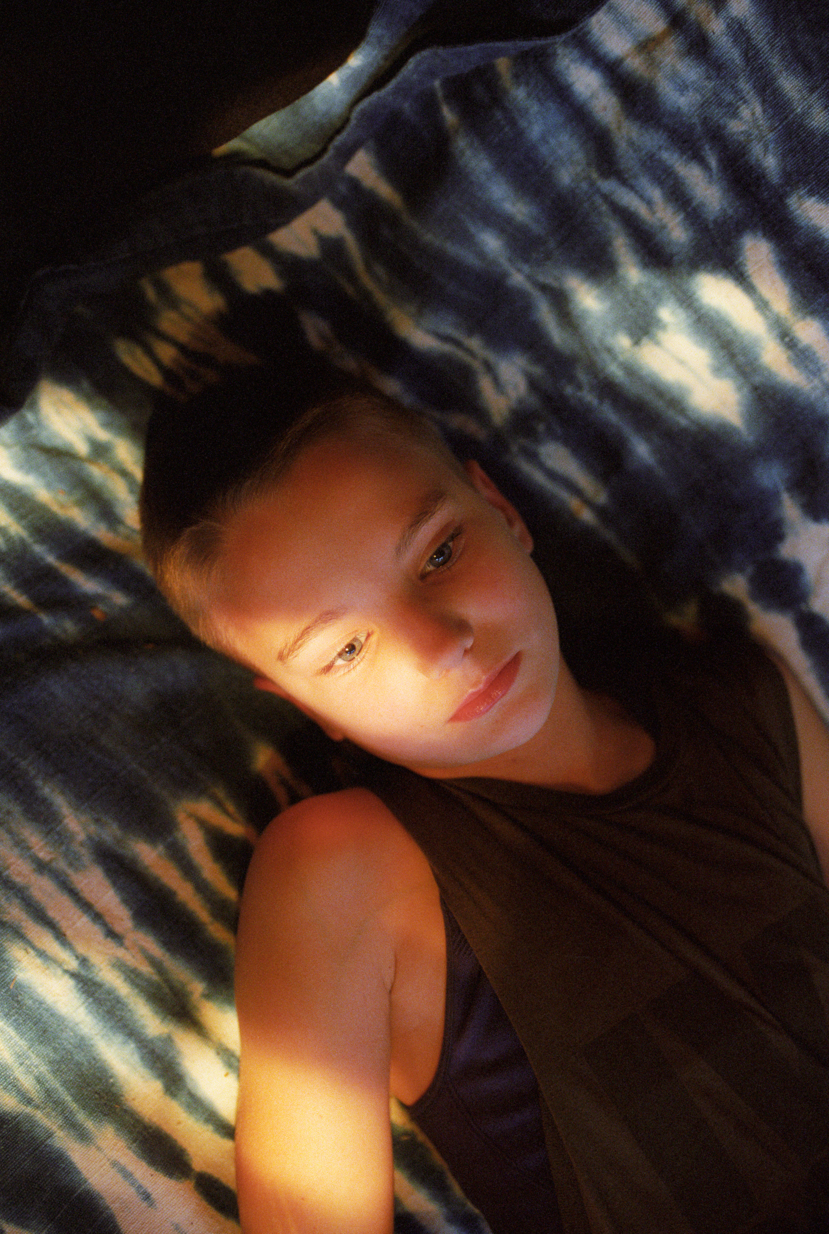 a person lays on a tie-dye bedspread with sunlight on their face