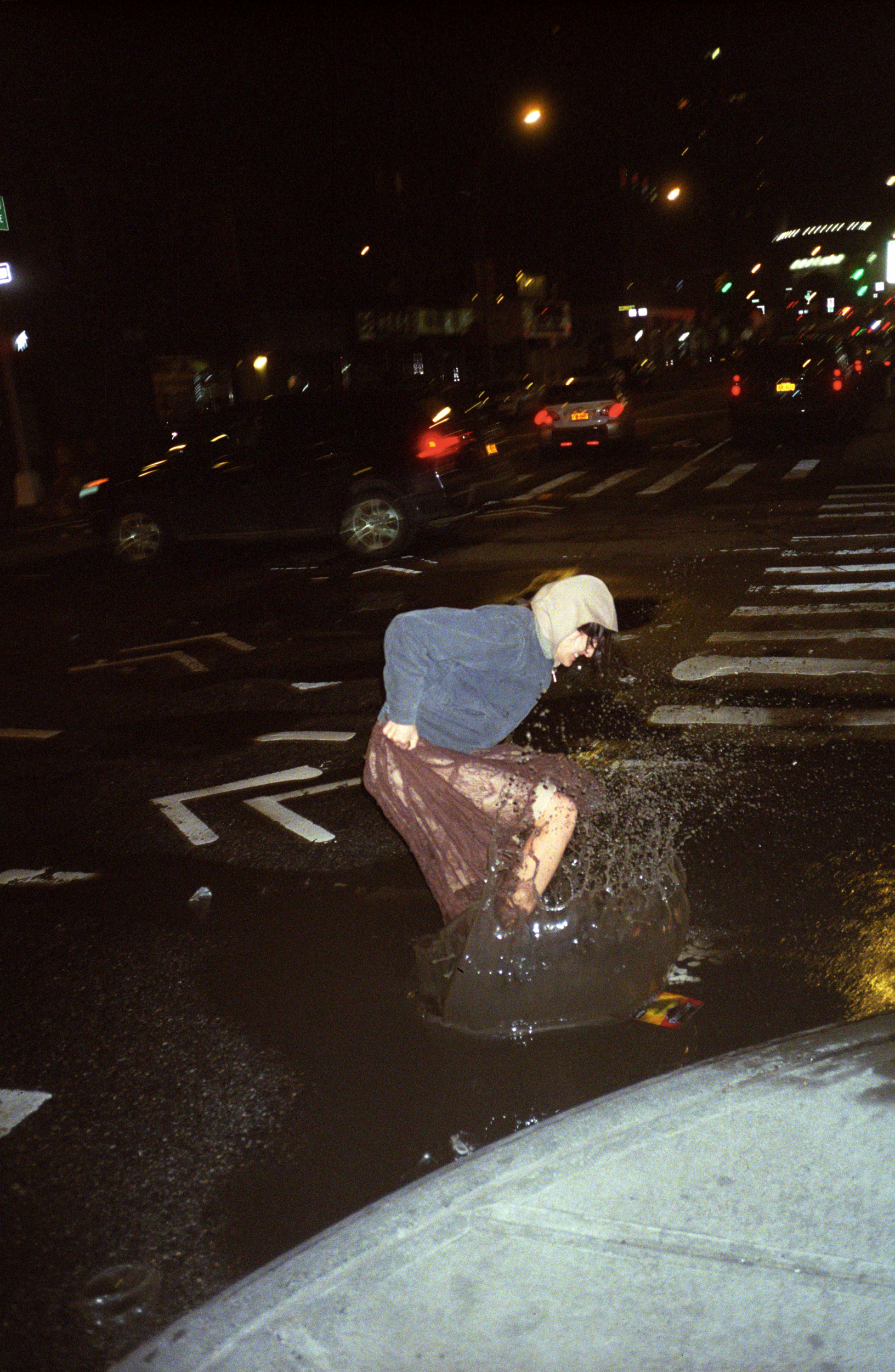 a person in a dress and hoodie splashes in a muddy NYC puddle