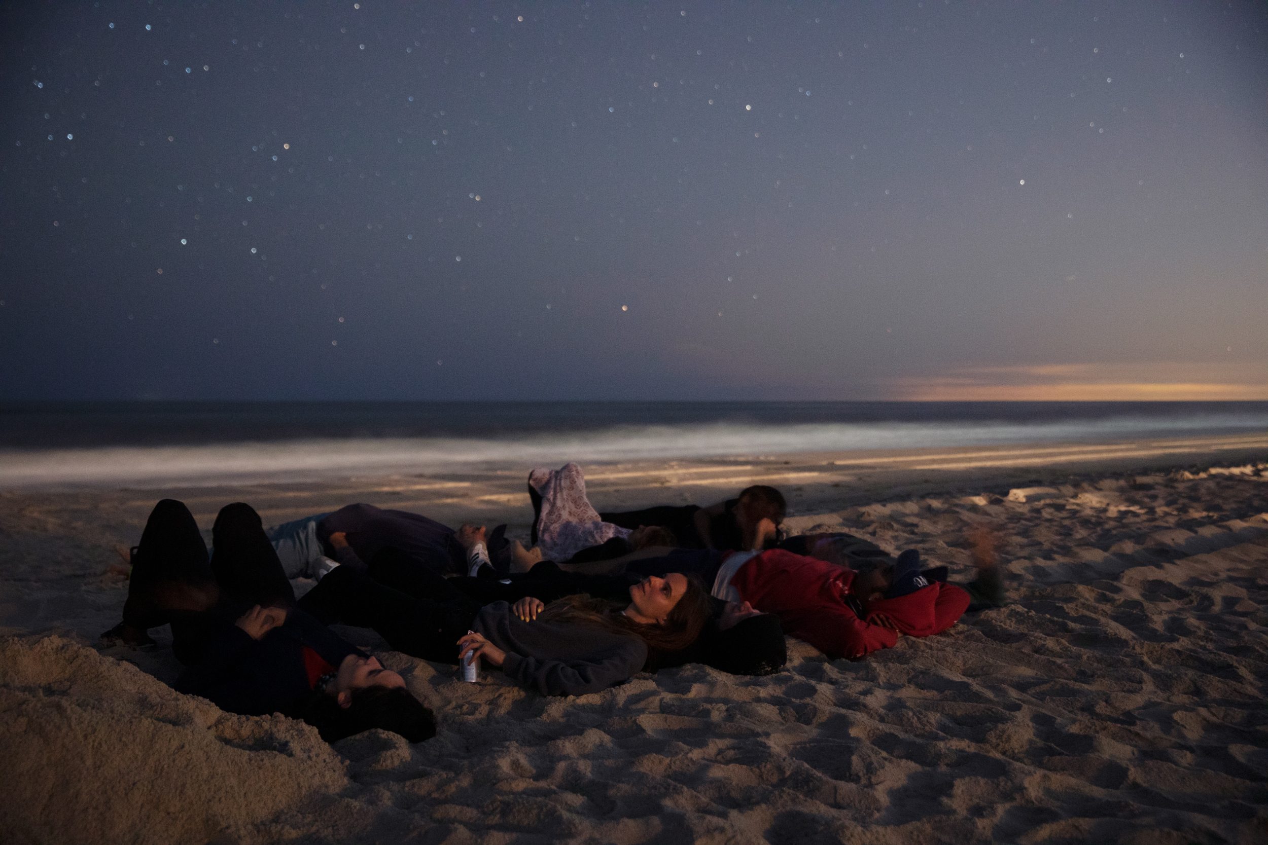 a group of people lay on the beach, looking at the stars 