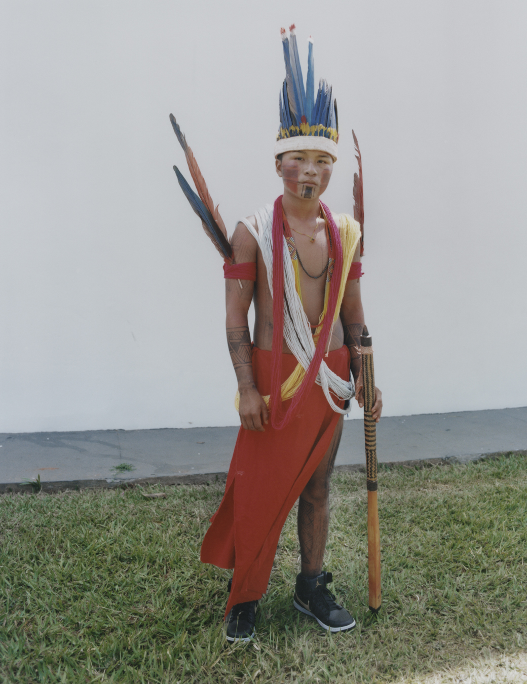 protester wearing traditional indigenous clothing standing against a wall and holding a spear.