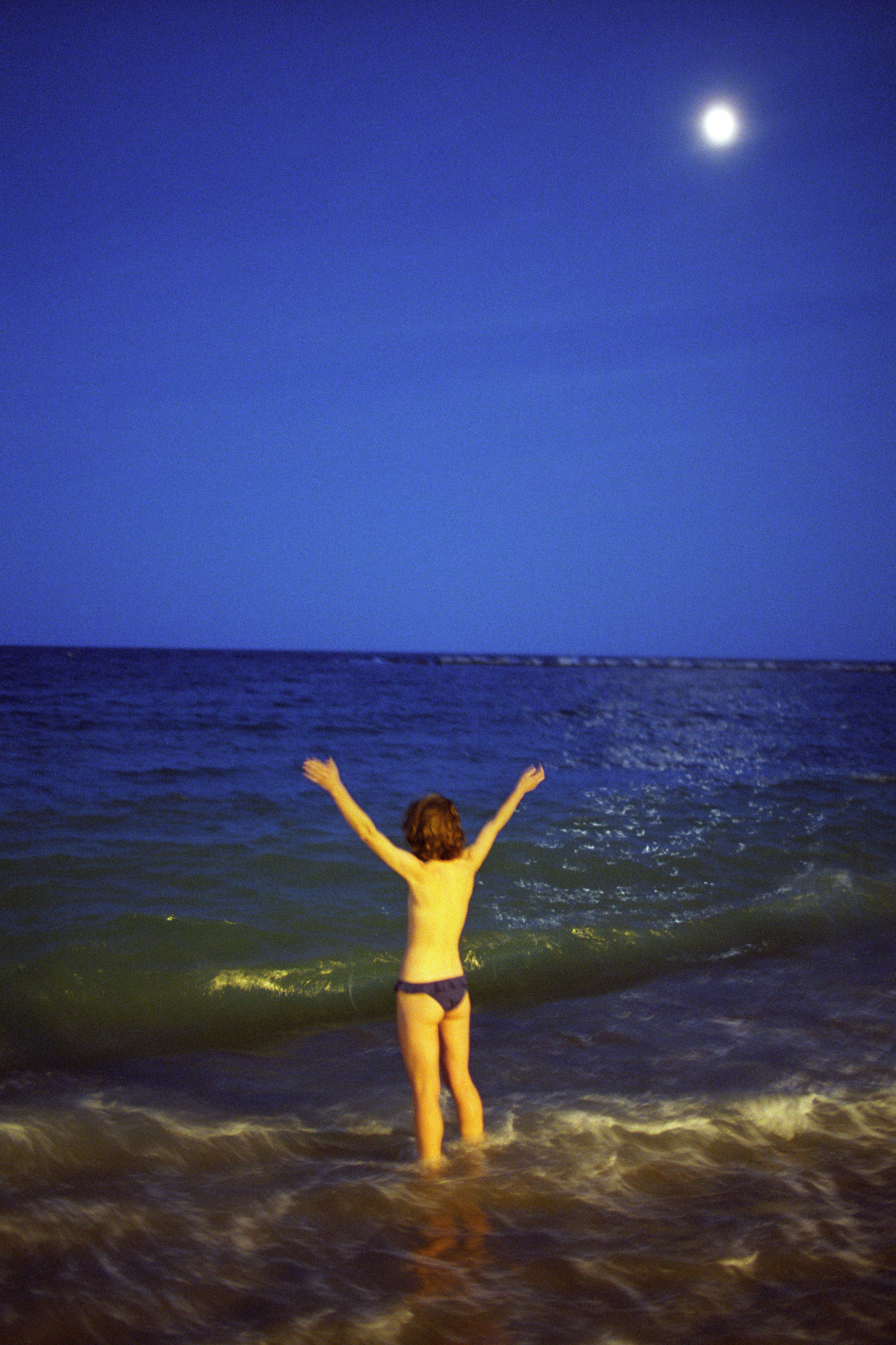 a person stands topless in the sea for a night with his arms in the air