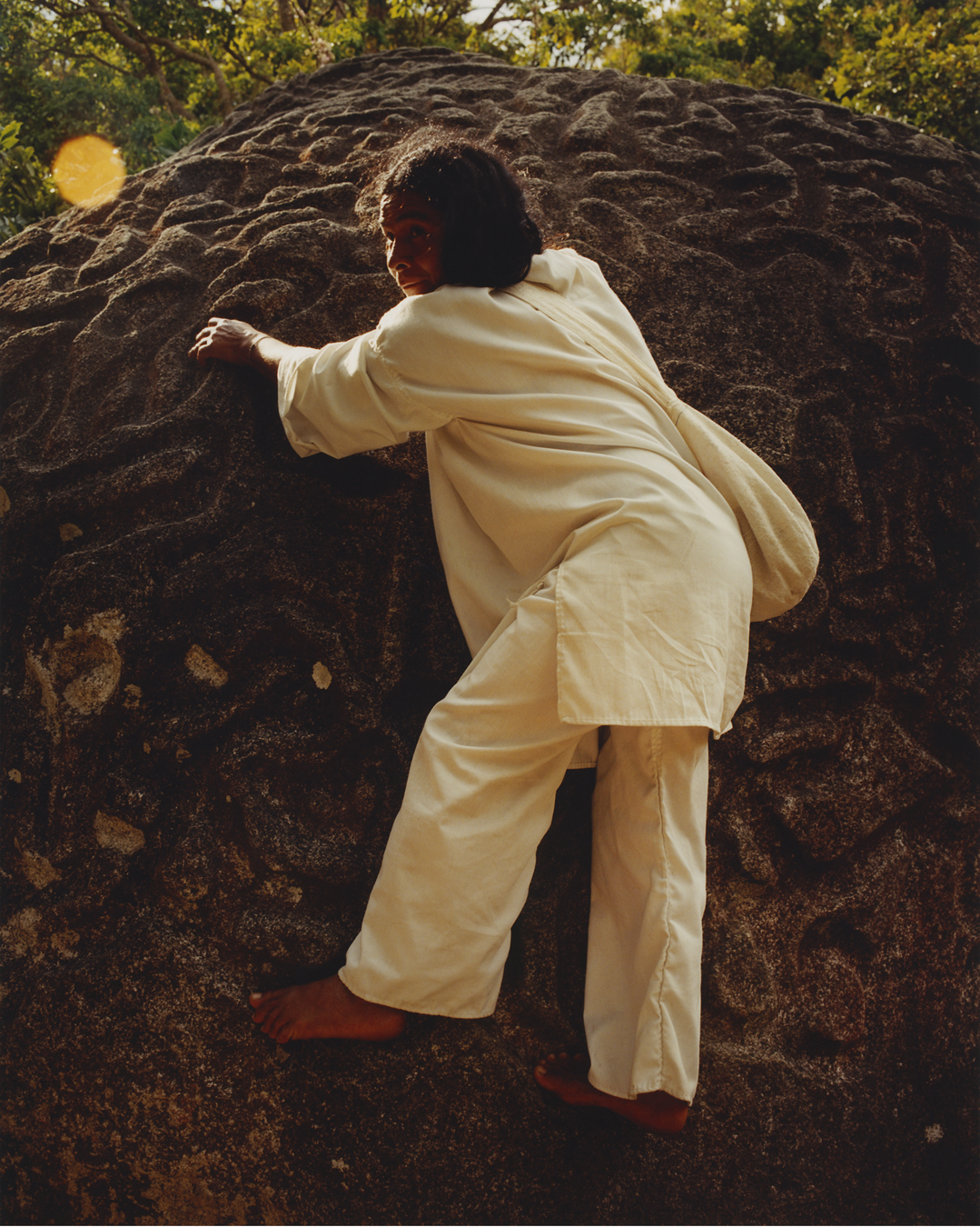 A man in white cotton clothing climbing a rock.