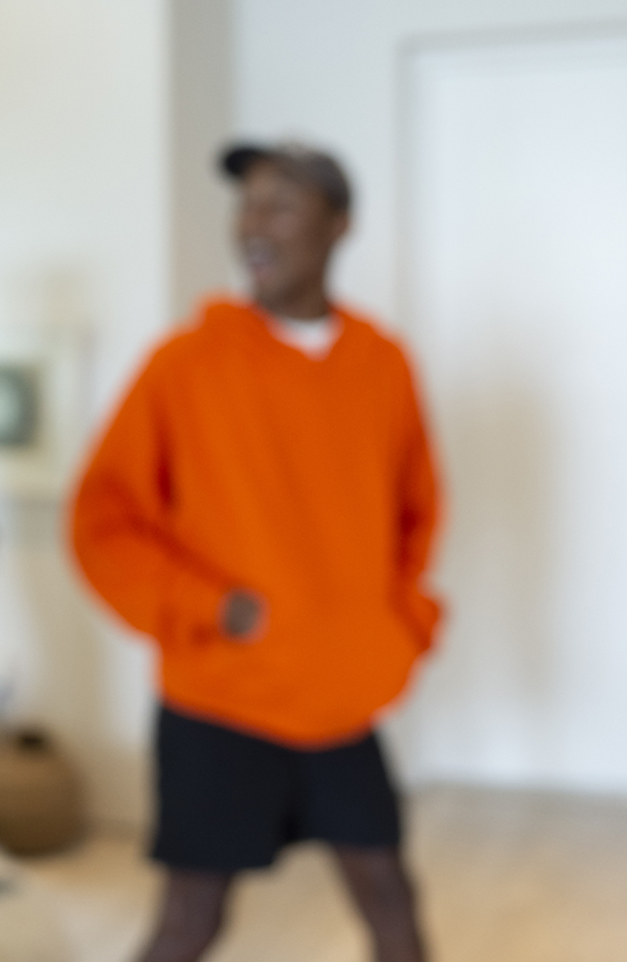 Fotografía borrosa de Pharrell Williams con una sudadera con capucha naranja y pantalones cortos negros 