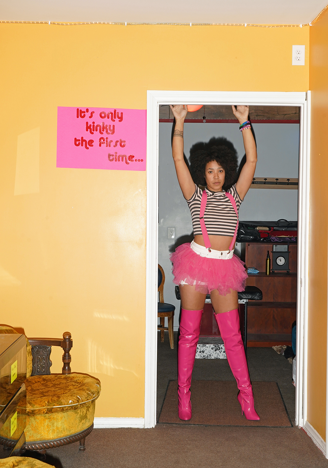 A woman in pink boots and a pink tutu stands next to a sign that says, 