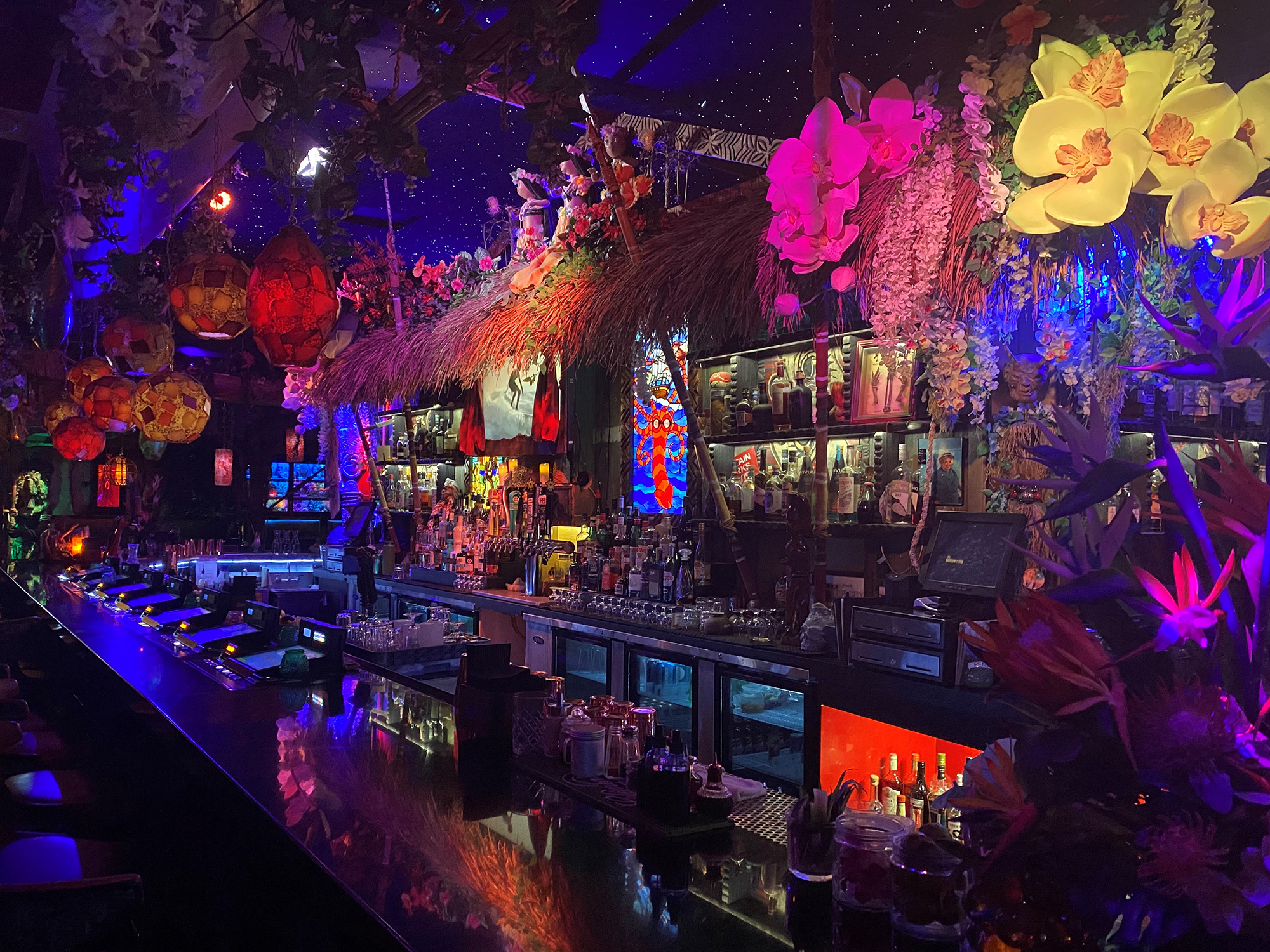 A colorfully lit tiki bar with many flowers and decorations