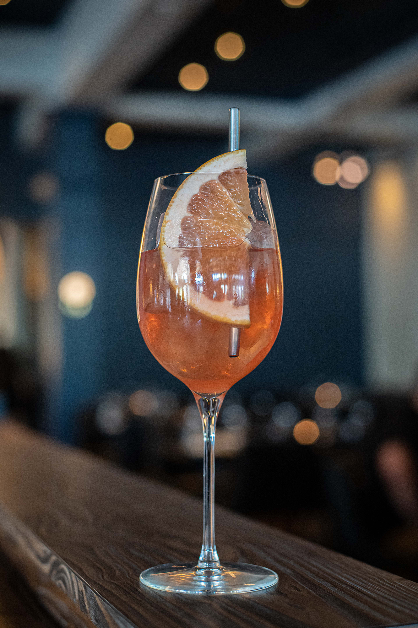 An orange mocktail in a stemmed glass with a slice of citrus and a metal straw called a Lavish Grove