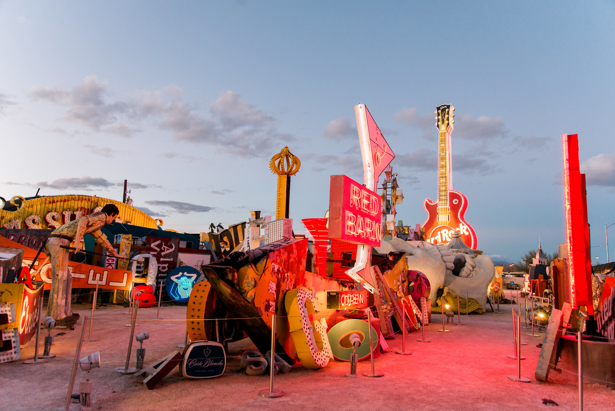 A photo of an arrangement of glowing antique neon signs at the Neon Museum against a dimming sky 