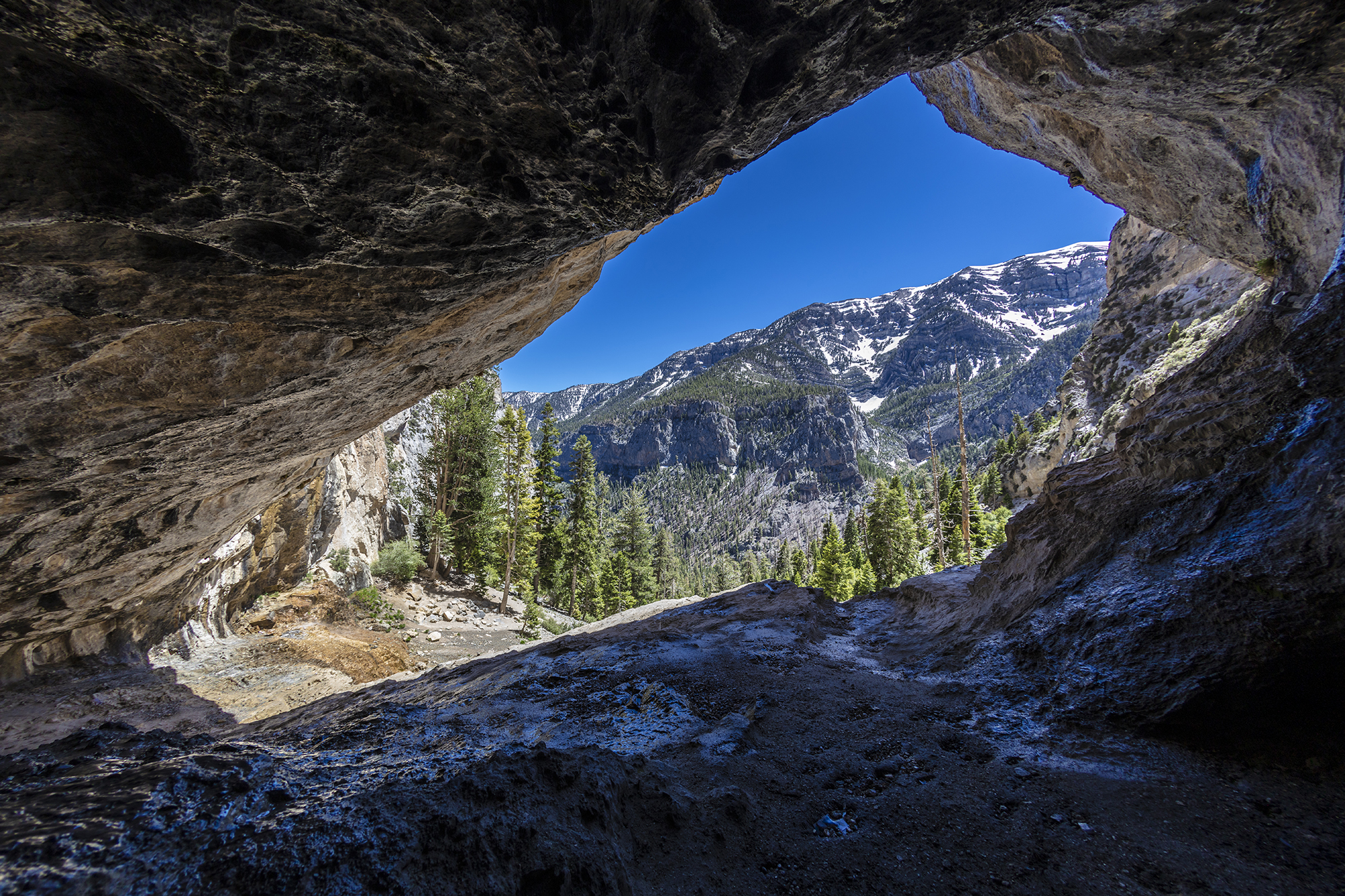 Photo of a view of Mt. Charleston, a snow-capped mountain, through a rocky cave.