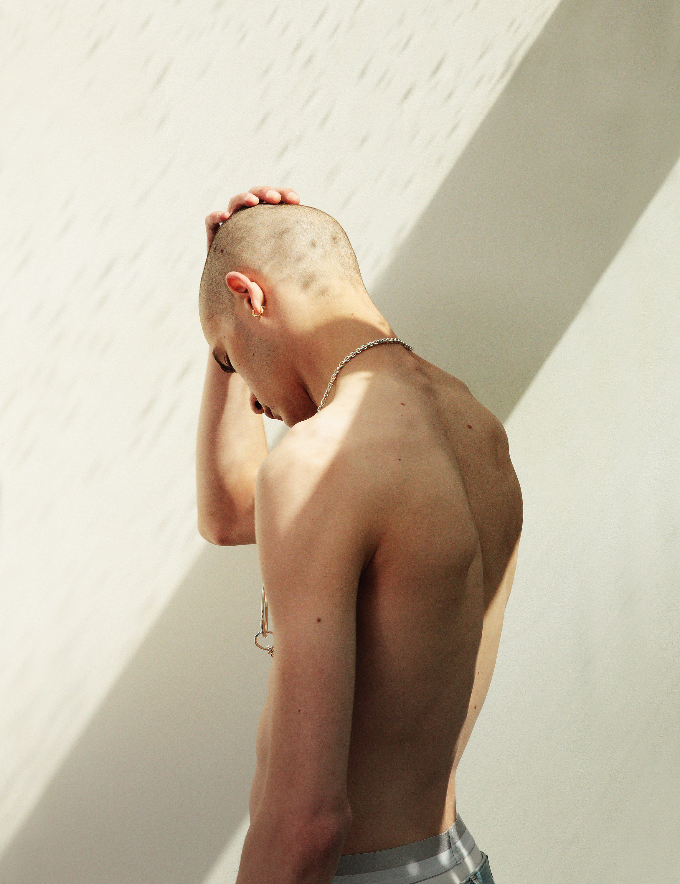 man with shaved head facing away from the camera against a white wall