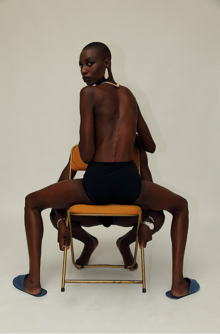 a topless woman shot from behind sitting on an orange chair 