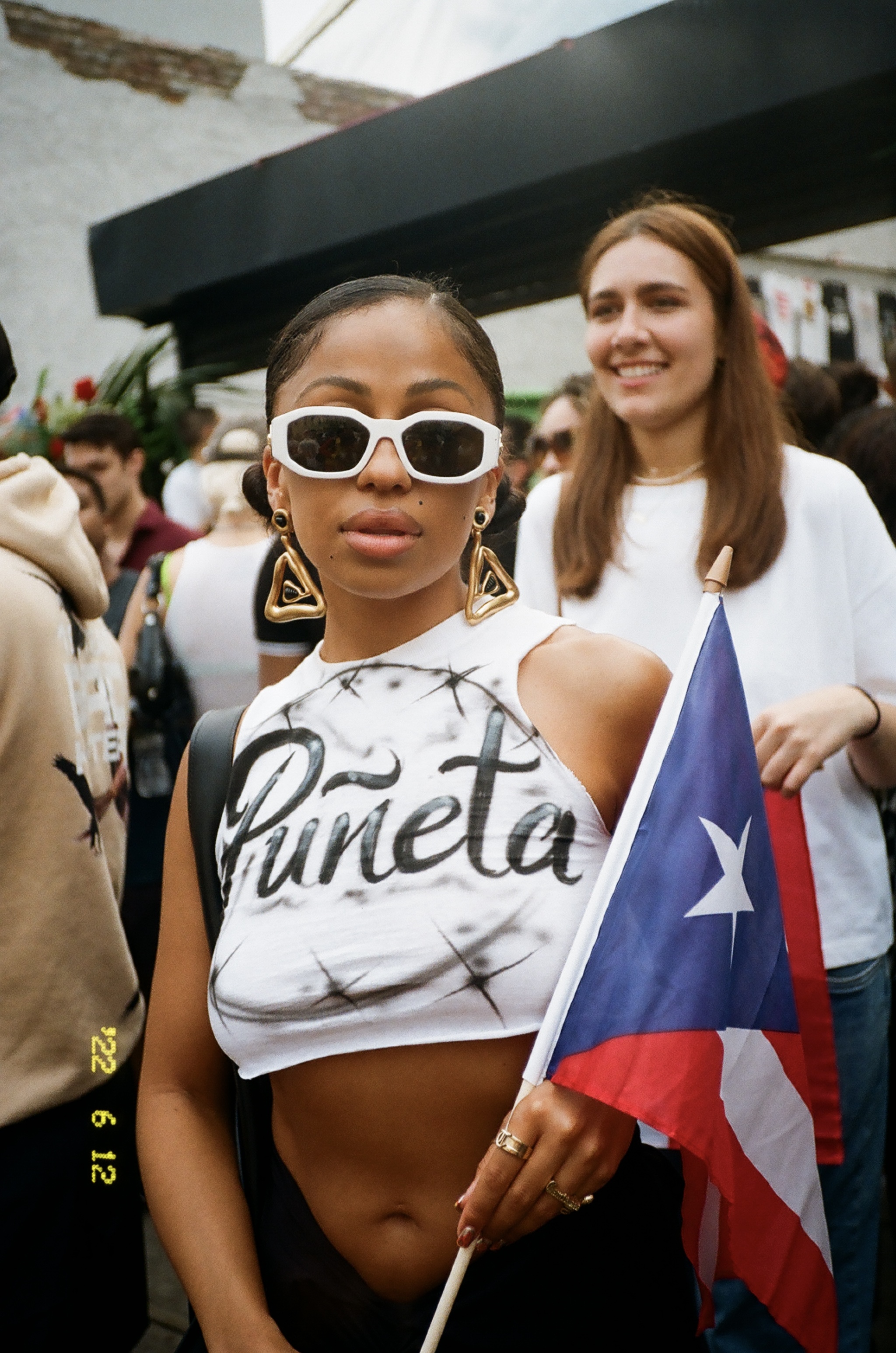 Woman in Bushwick wearing sunglasses, white Puñeta t-shirt, carrying the Puerto Rican flag