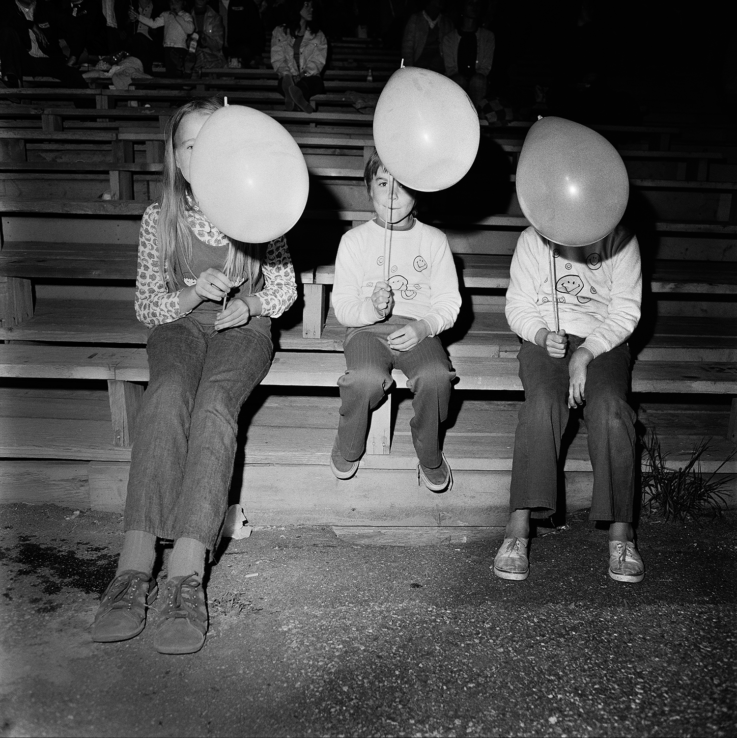 Tiga orang anak duduk sambil memegang balon