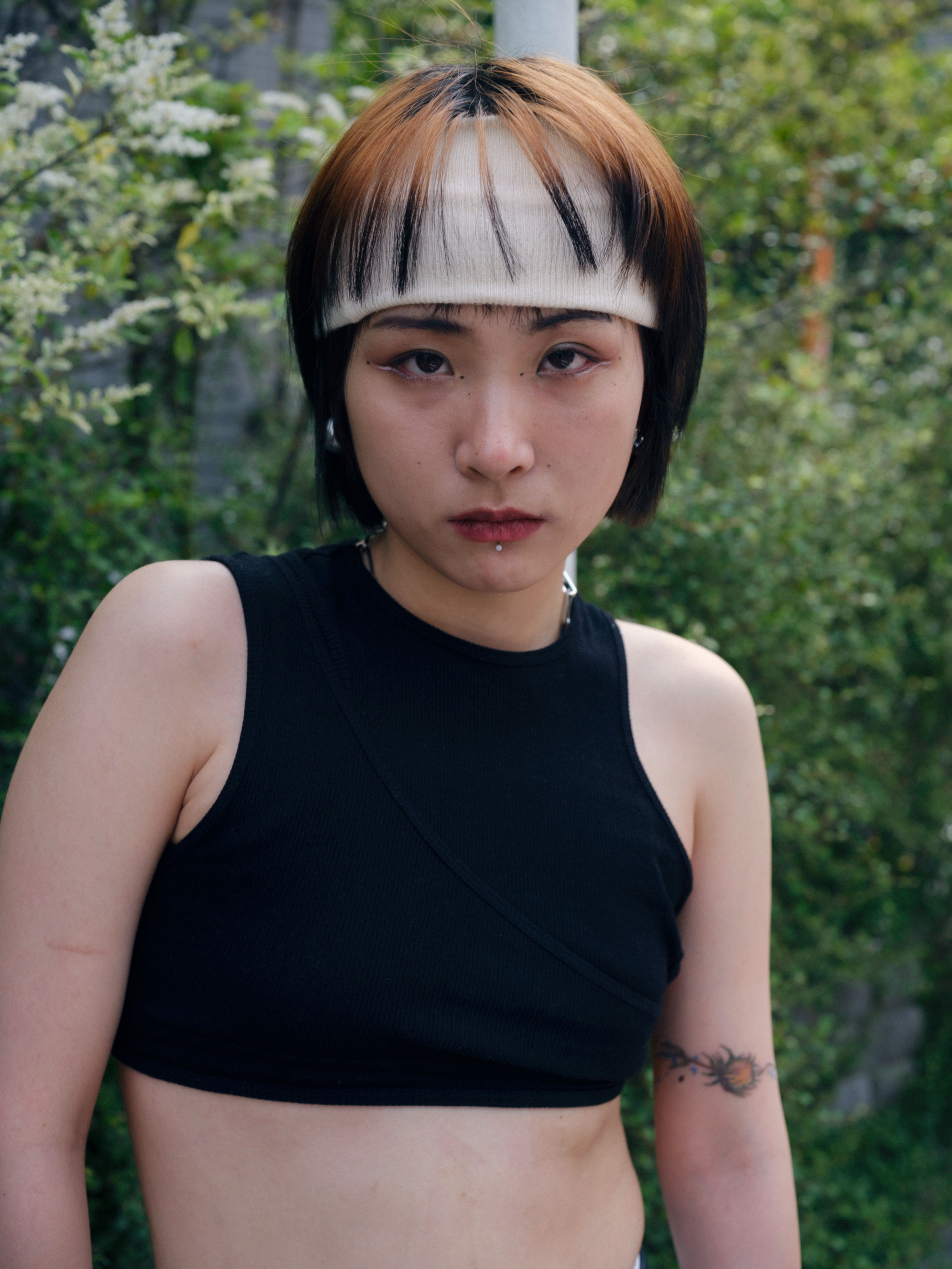a person wearing a black cropped tank top with a white sweatband around their head, under dyed peach-coloured hair