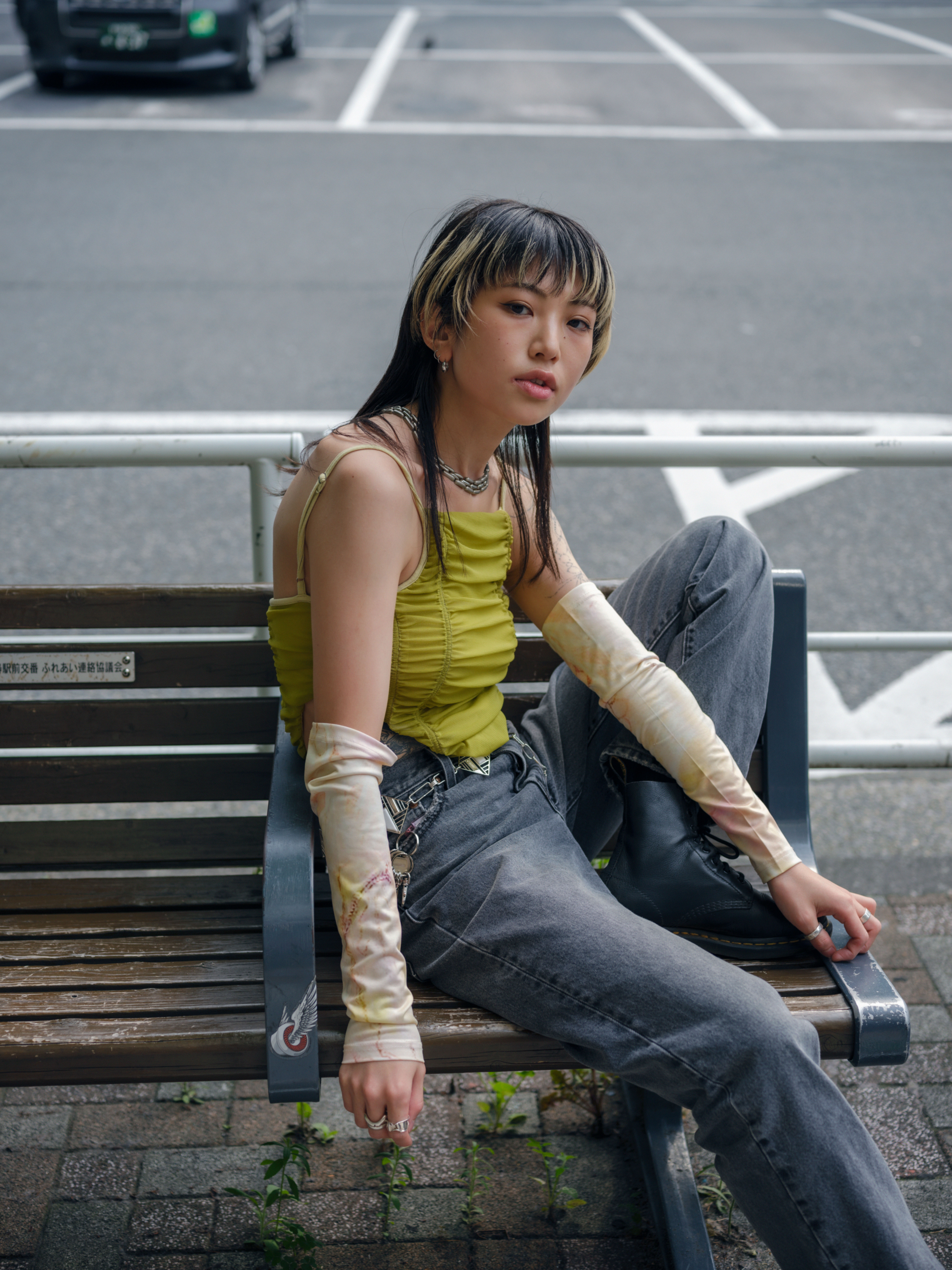 a person wearing jeans and a wrinkled green blouse (with bleached streaks in the hair) sits casually on a bench in tokyo
