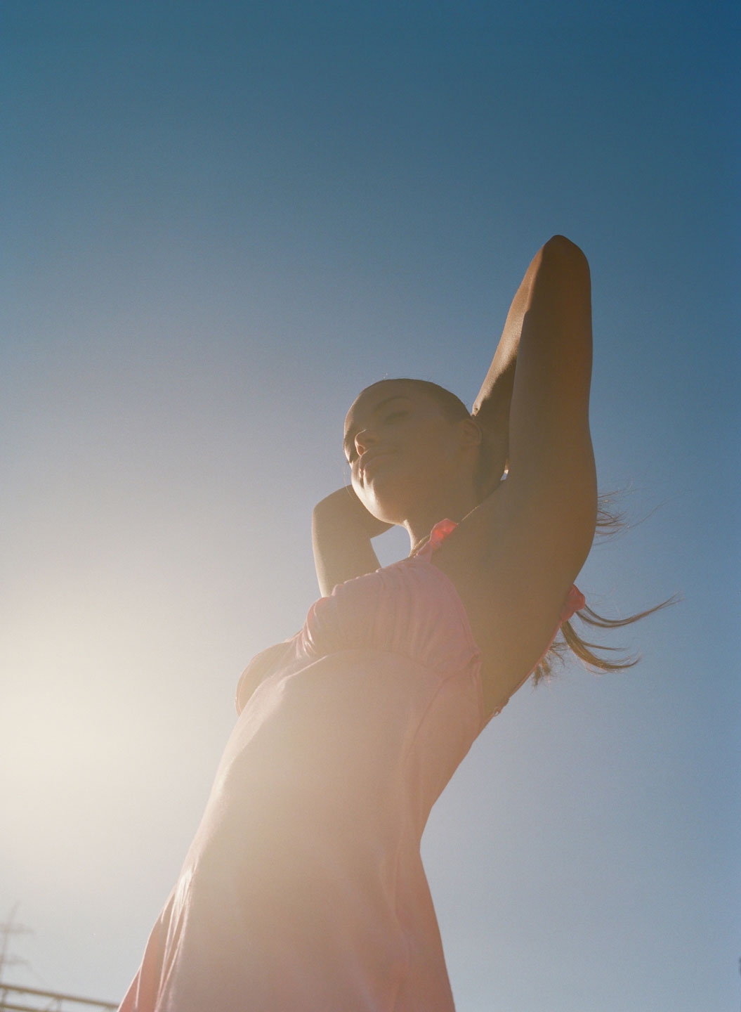 ella balinska standing in the sun, with her arms behind her head, shot from below