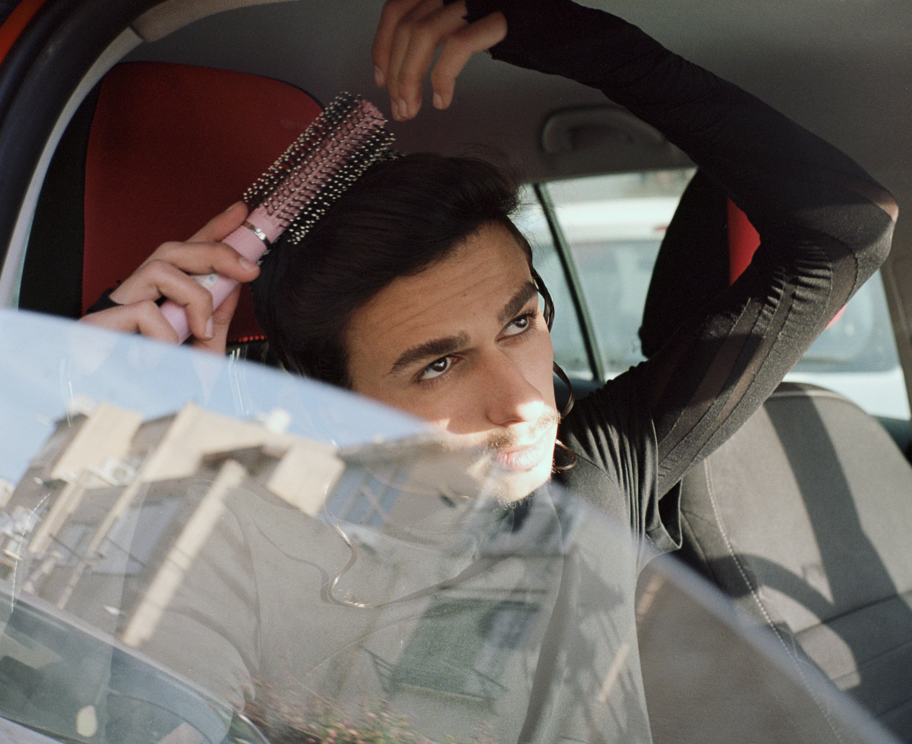 Un jeune juif orthodoxe se coiffe avec une brosse rose sur le siège avant d'une voiture.