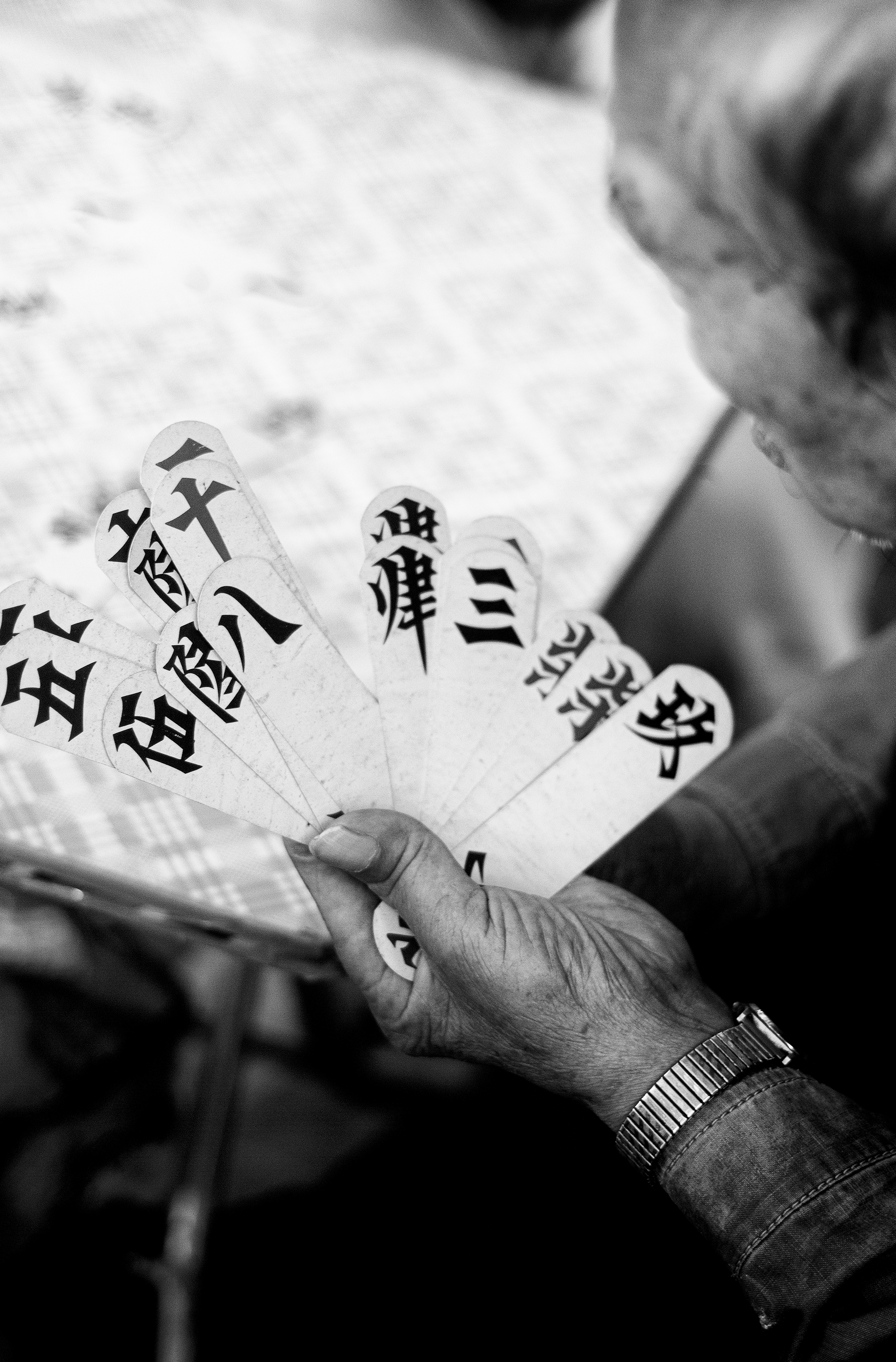 a wrinkled hand holds a splayed array of cards bearing chinese symbols