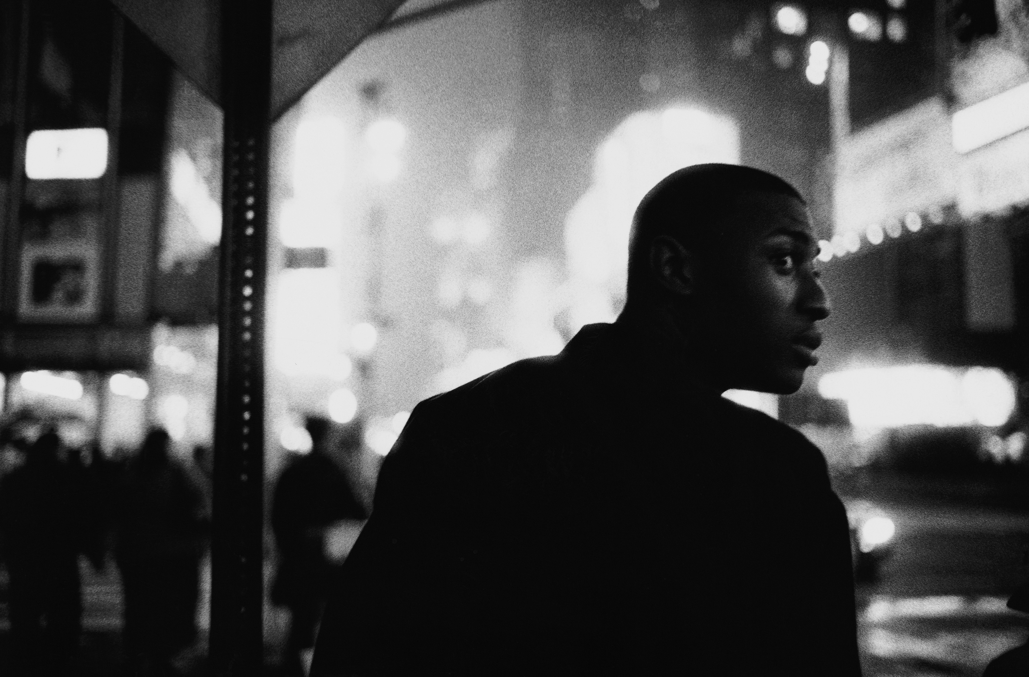a man peers over his shoulder in a busy nighttime street scene