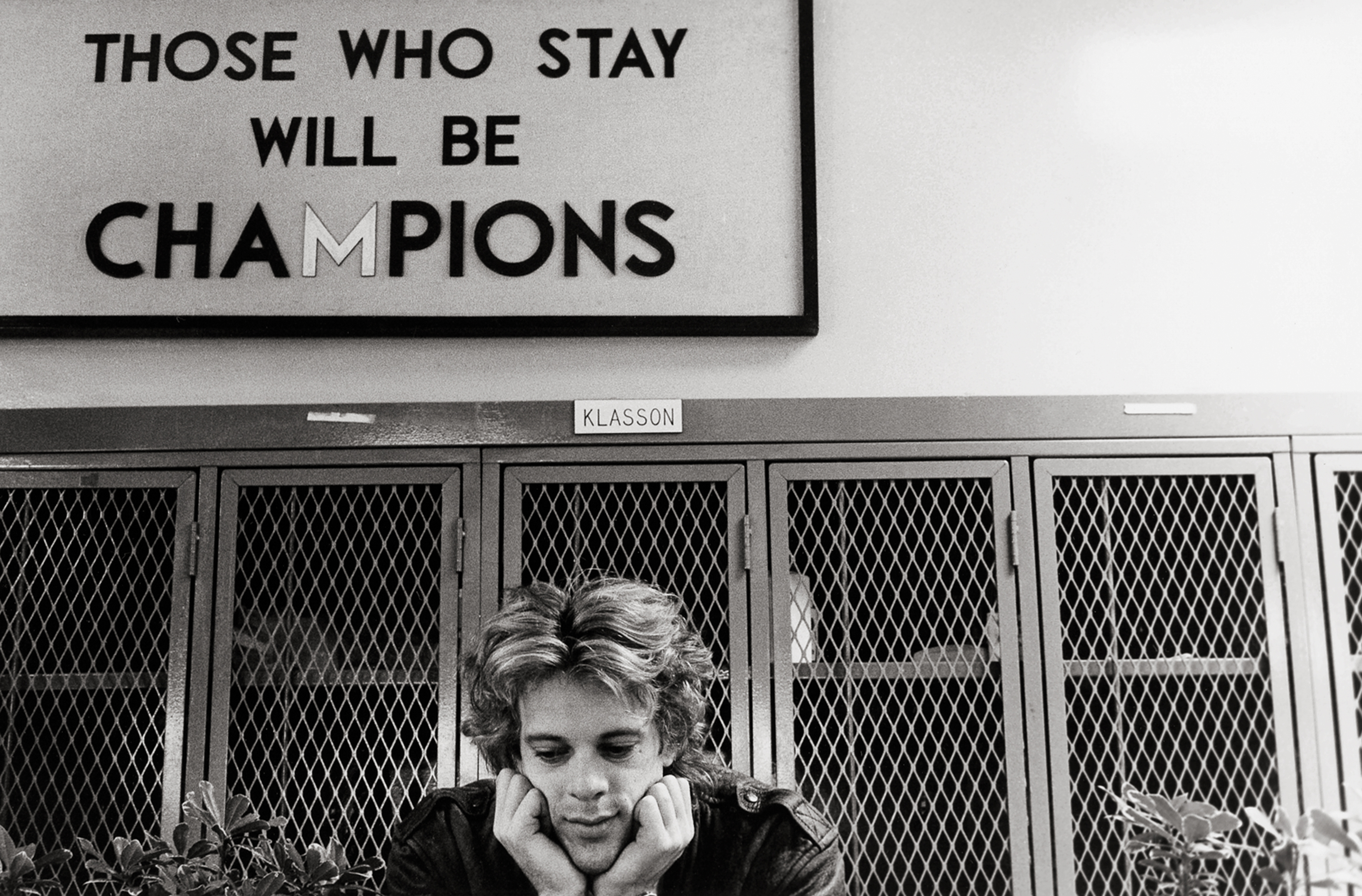 a man sits with his head in his hands, below a sign proclaiming 'THOSE WHO STAY WILL BE CHAMPIONS'