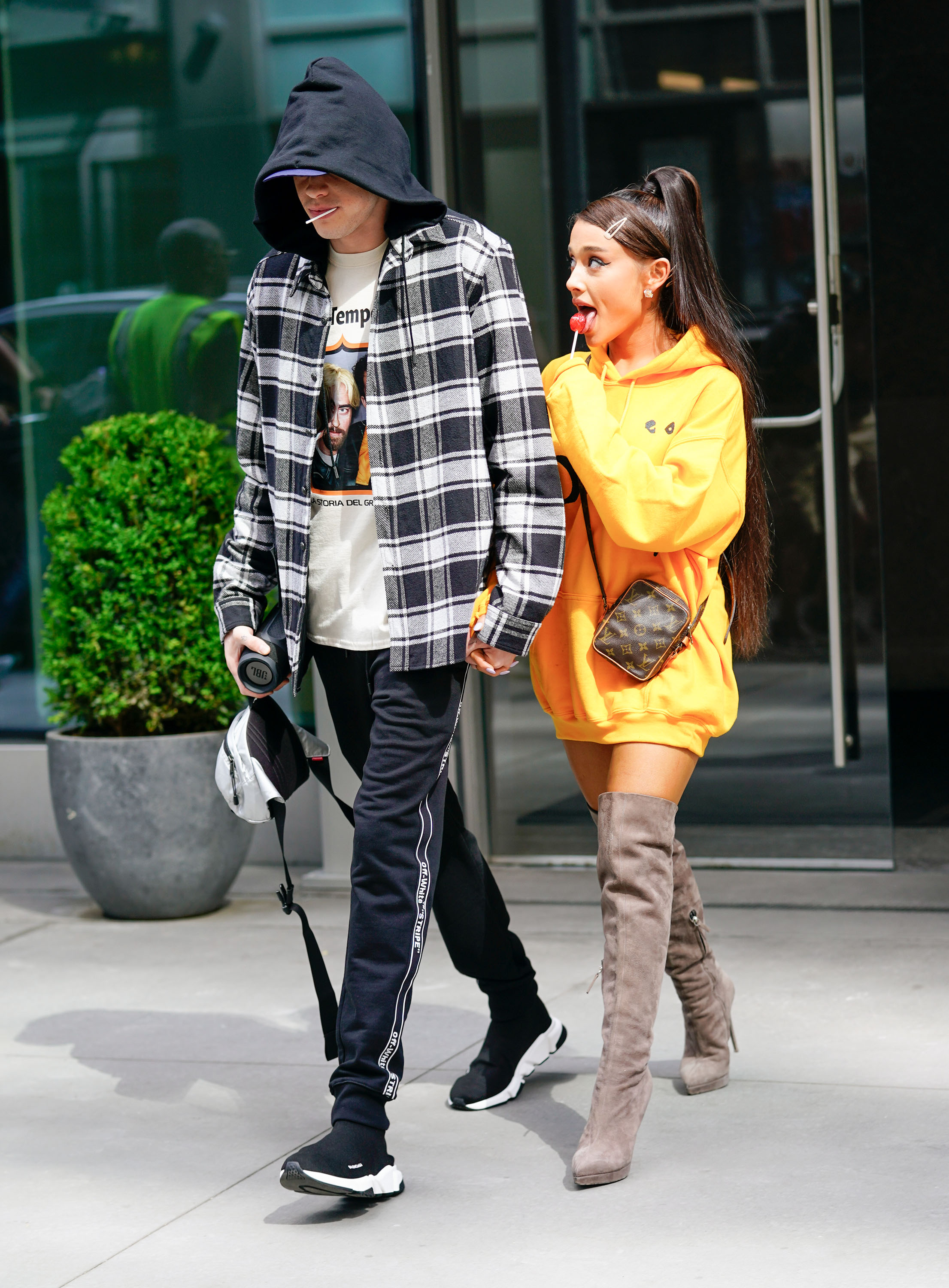 Ariana Grande wearing an oversized hoodie and boots and licking a lollipop on the streets of New York with Pete Davidson in 2018