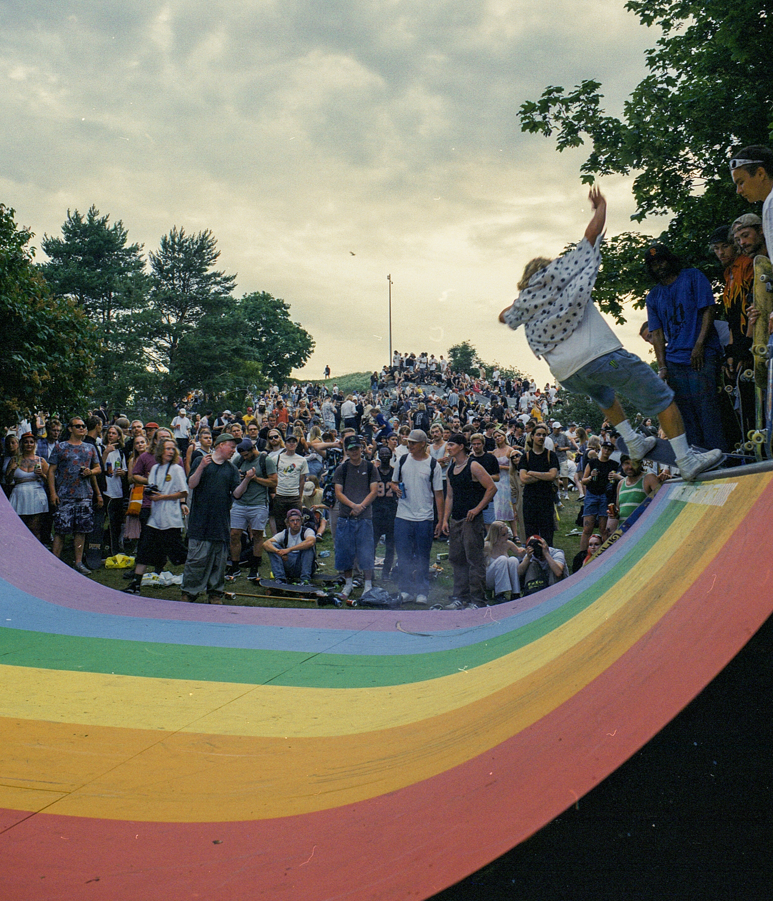 people watching skateboarders on a rainbow coloured ramp