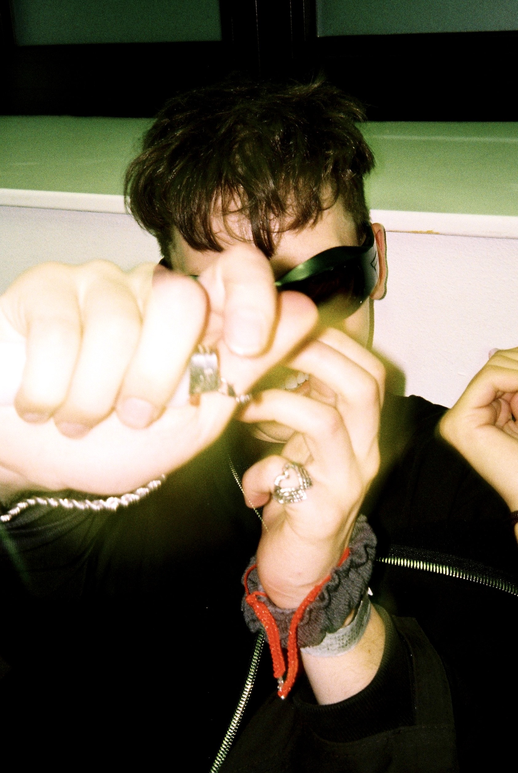 someone with rings, jewellery and black clothing hiding their face from the camera smiling