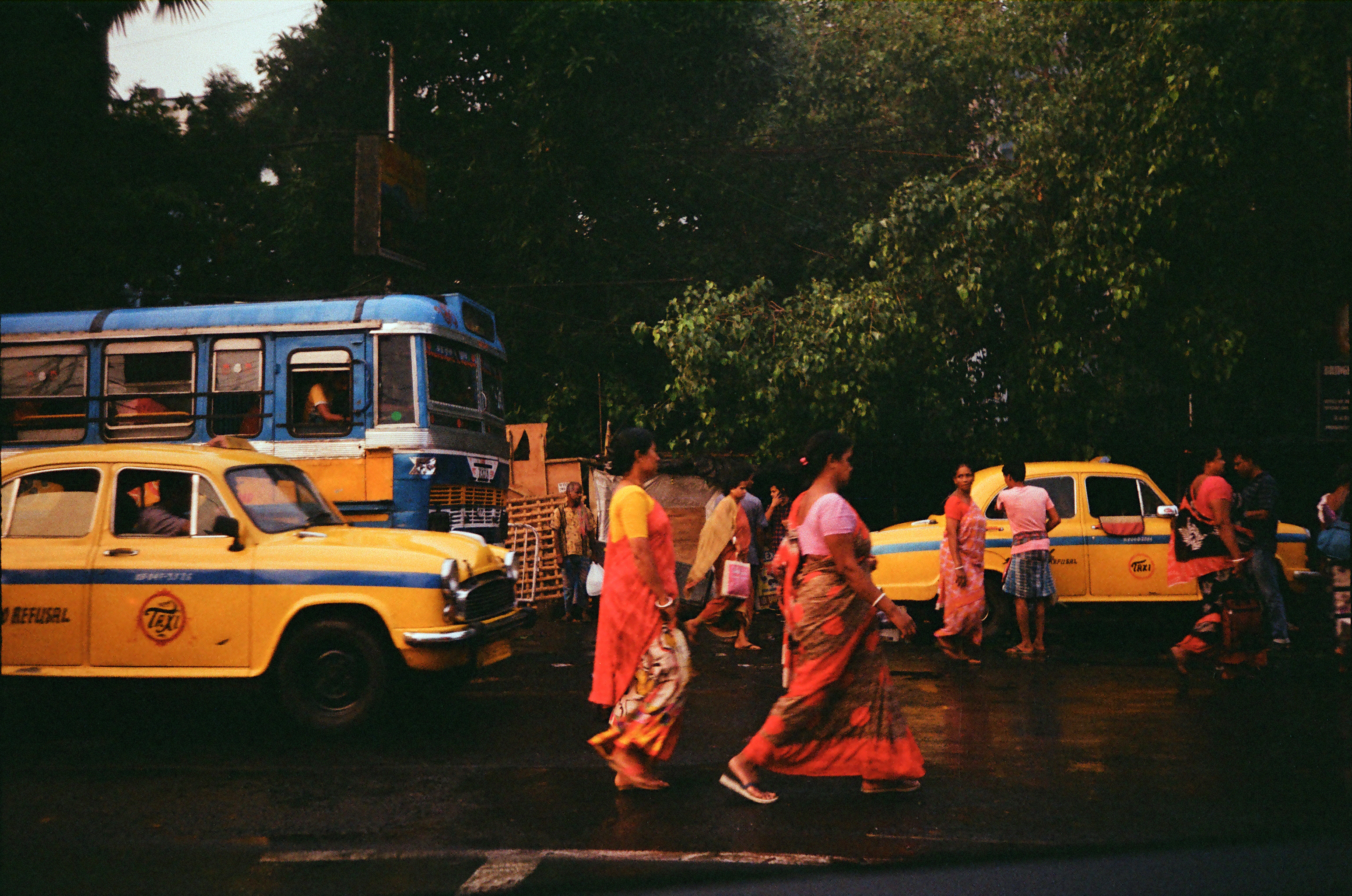 People walking across the street amongst taxis and buses.