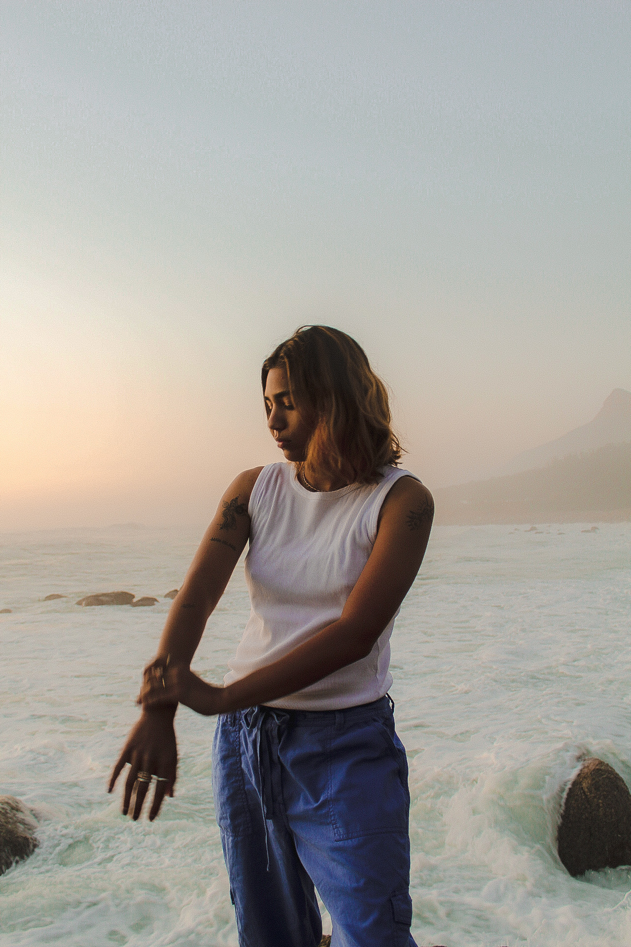 Person in a vest standing in the shallow ocean crashing against the rocks at sun set