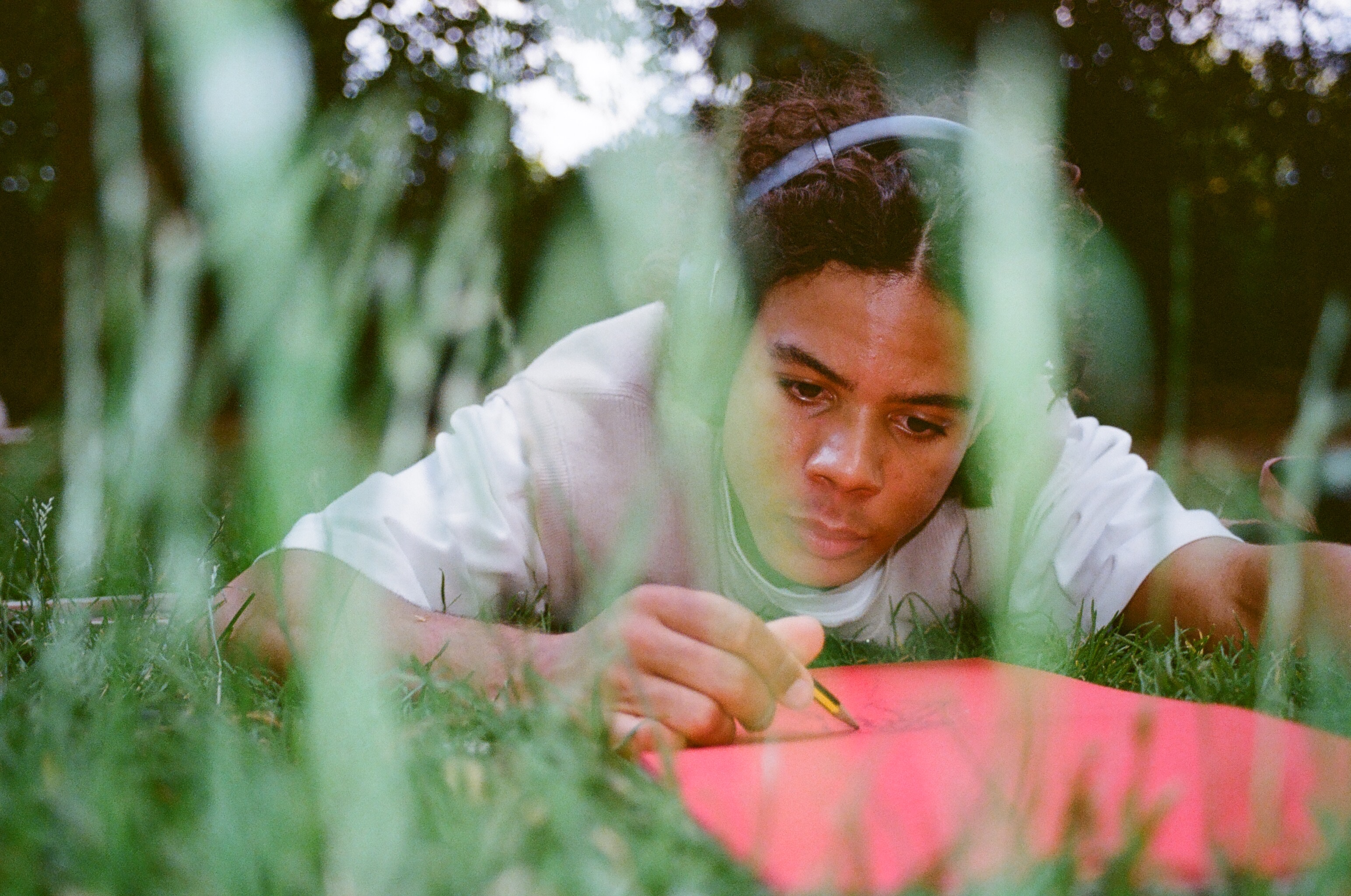 Person laying in the grass drawing on red paper