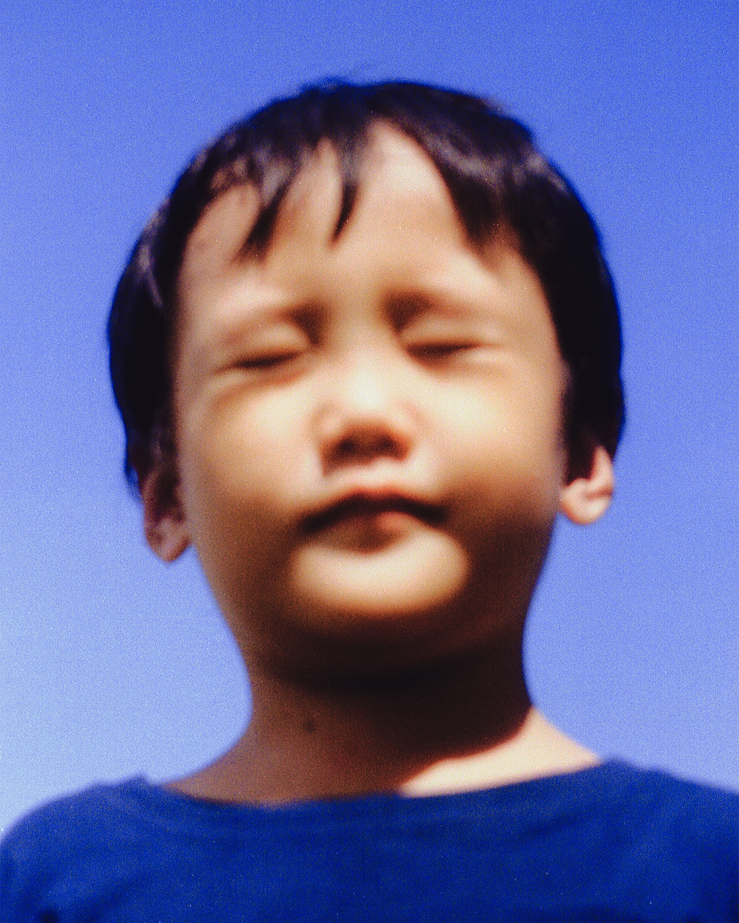 A young boy in a blue top squinting in the sun