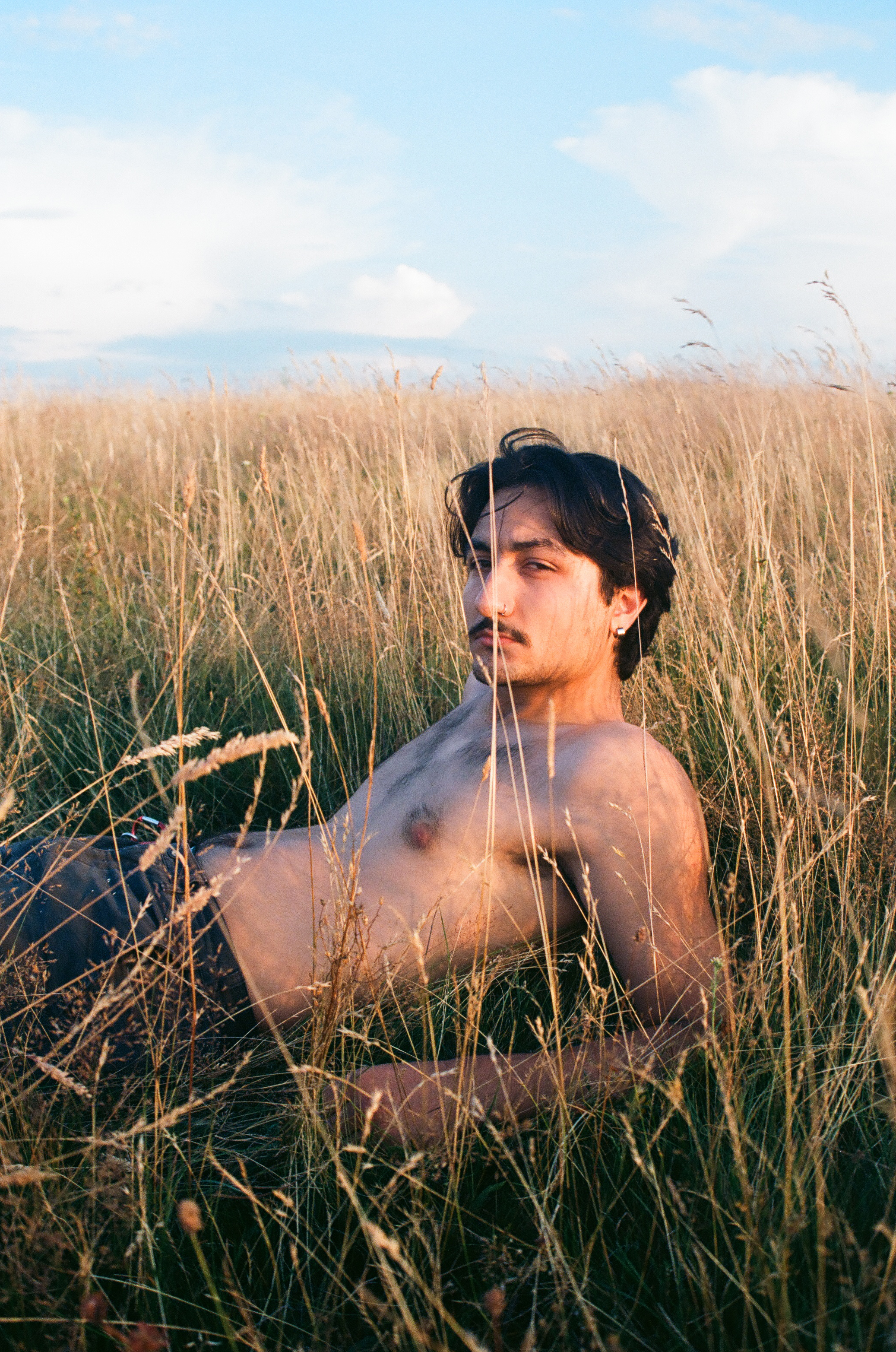 shirtless man sitting amongst the wheat fields