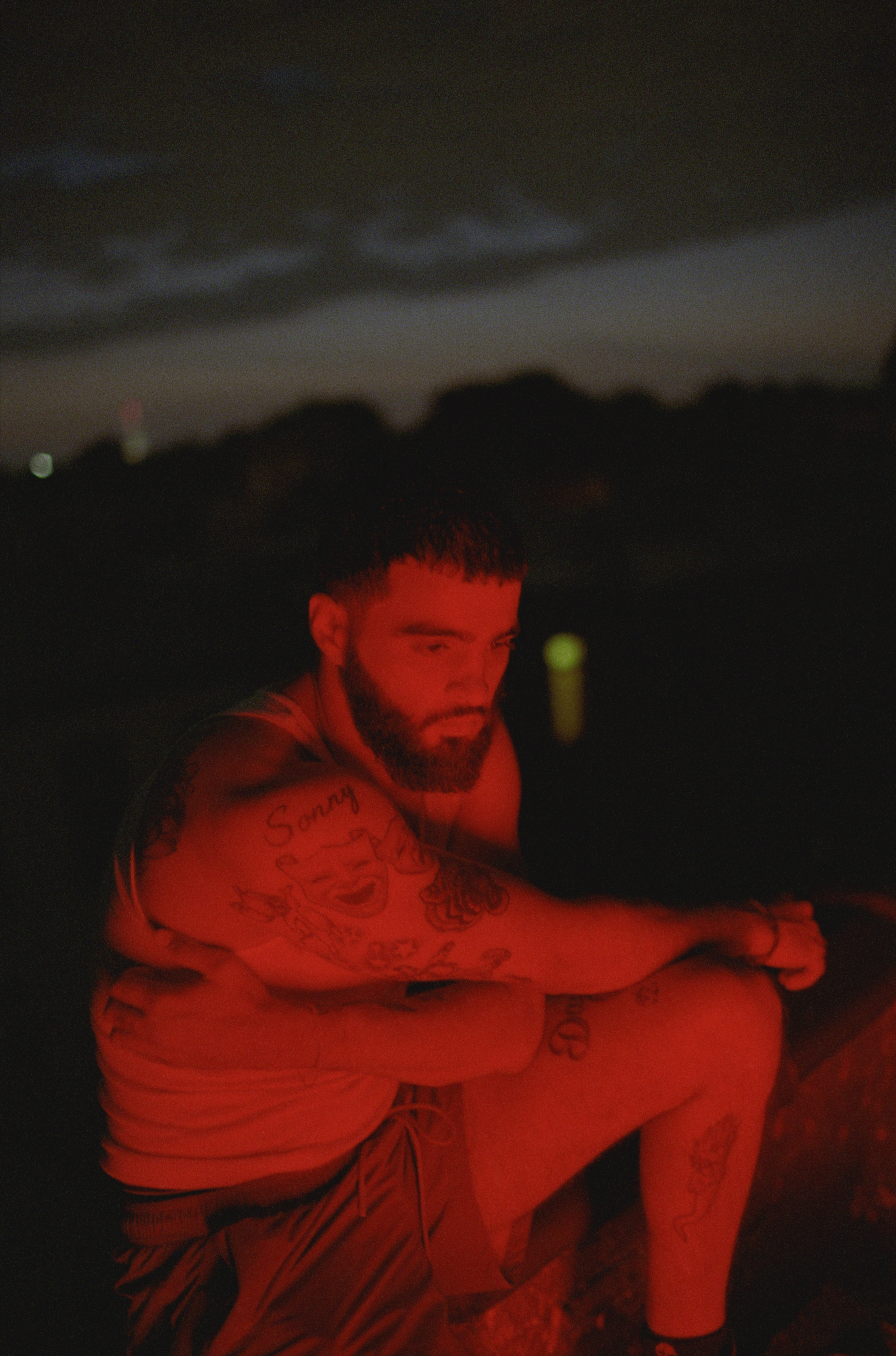 man stretching in a vest and shorts sitting on a roof under a red light