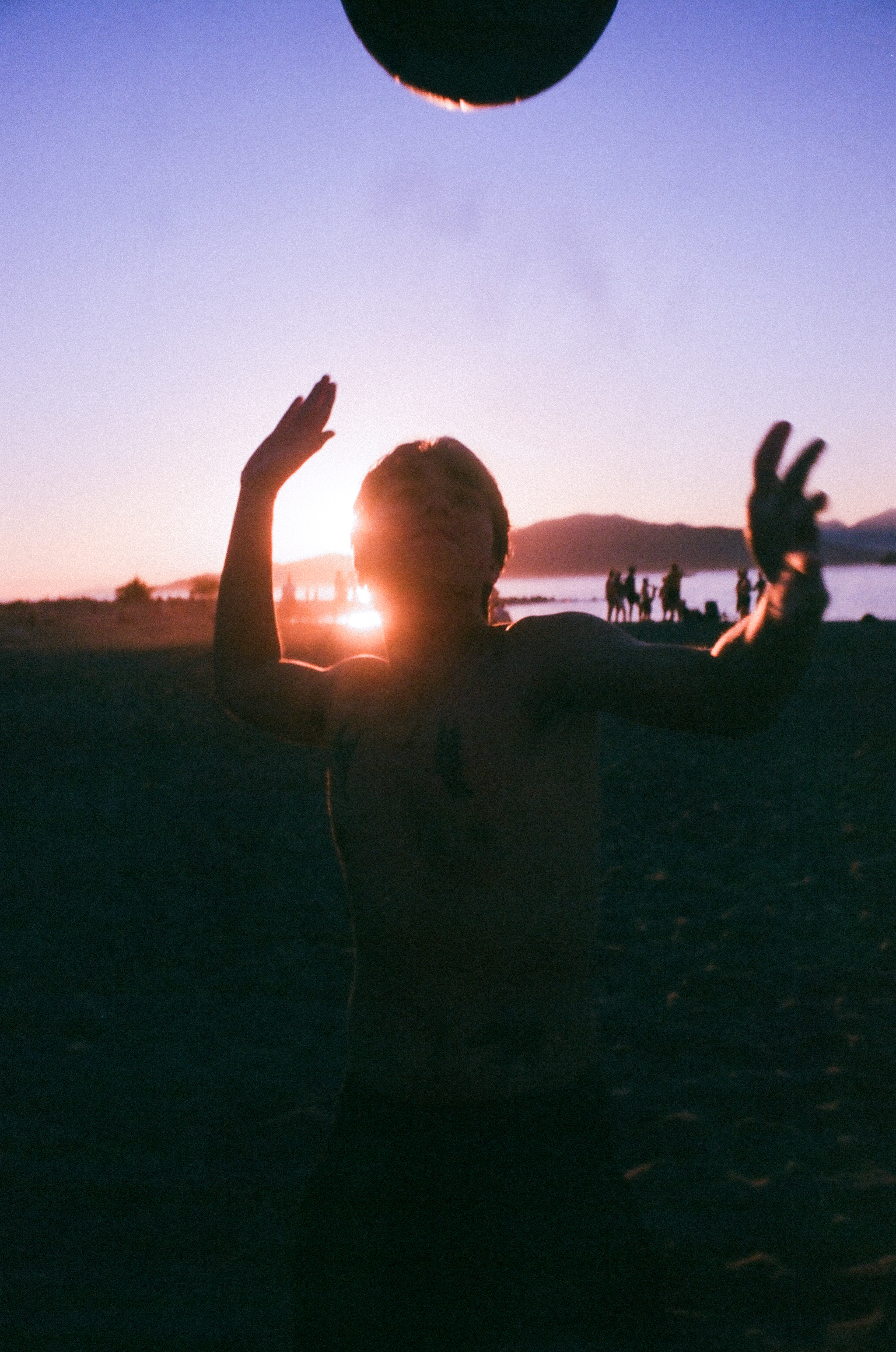 Shirtless man dancing on the beach as the sun sets