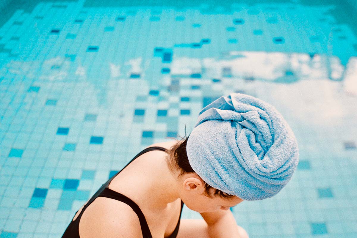 Girl in a bathing suit and towel on her head at a pool in east London