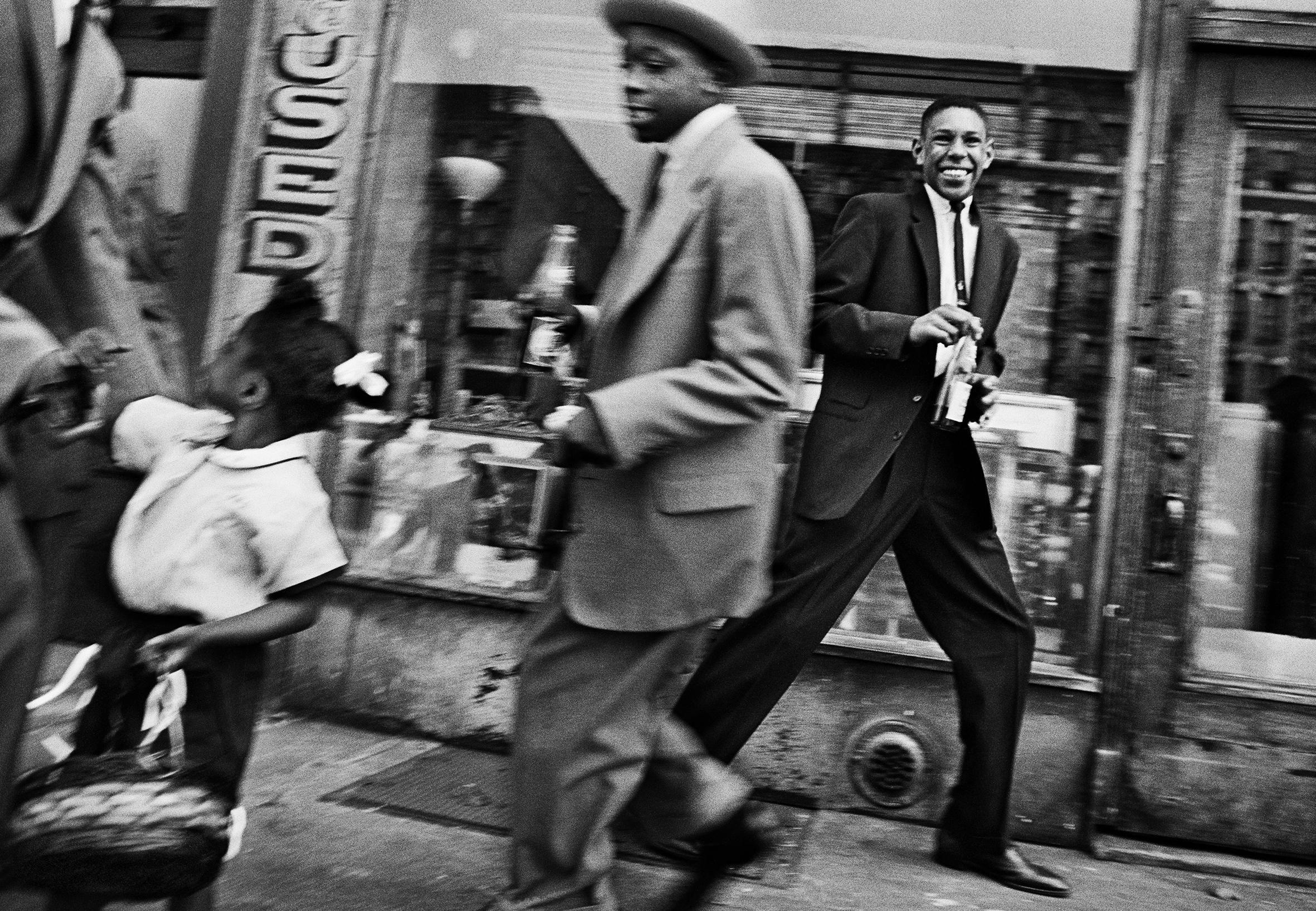 Black-and-white photo of two people in suits dancing outside of a store in Harlem