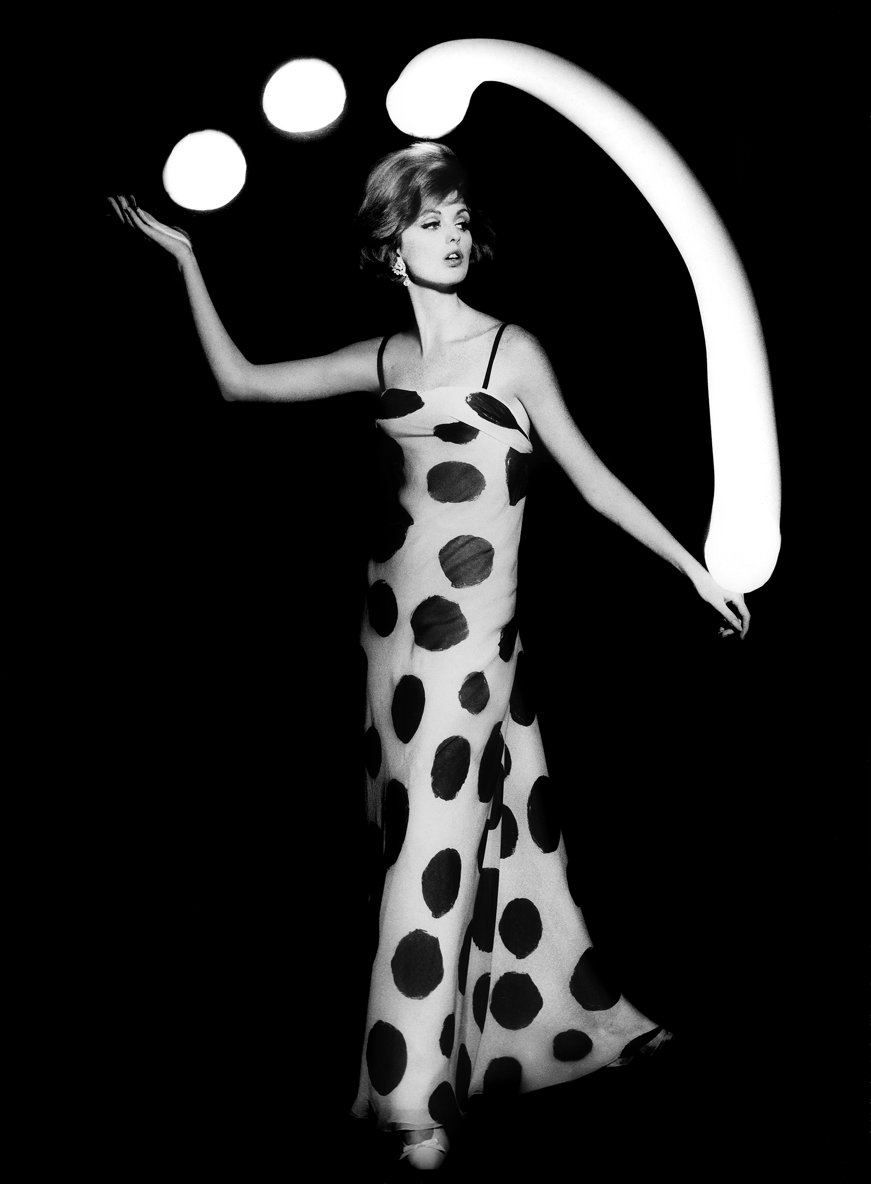 Black-and-white photo of a woman in a polka dot dress juggling white light balls