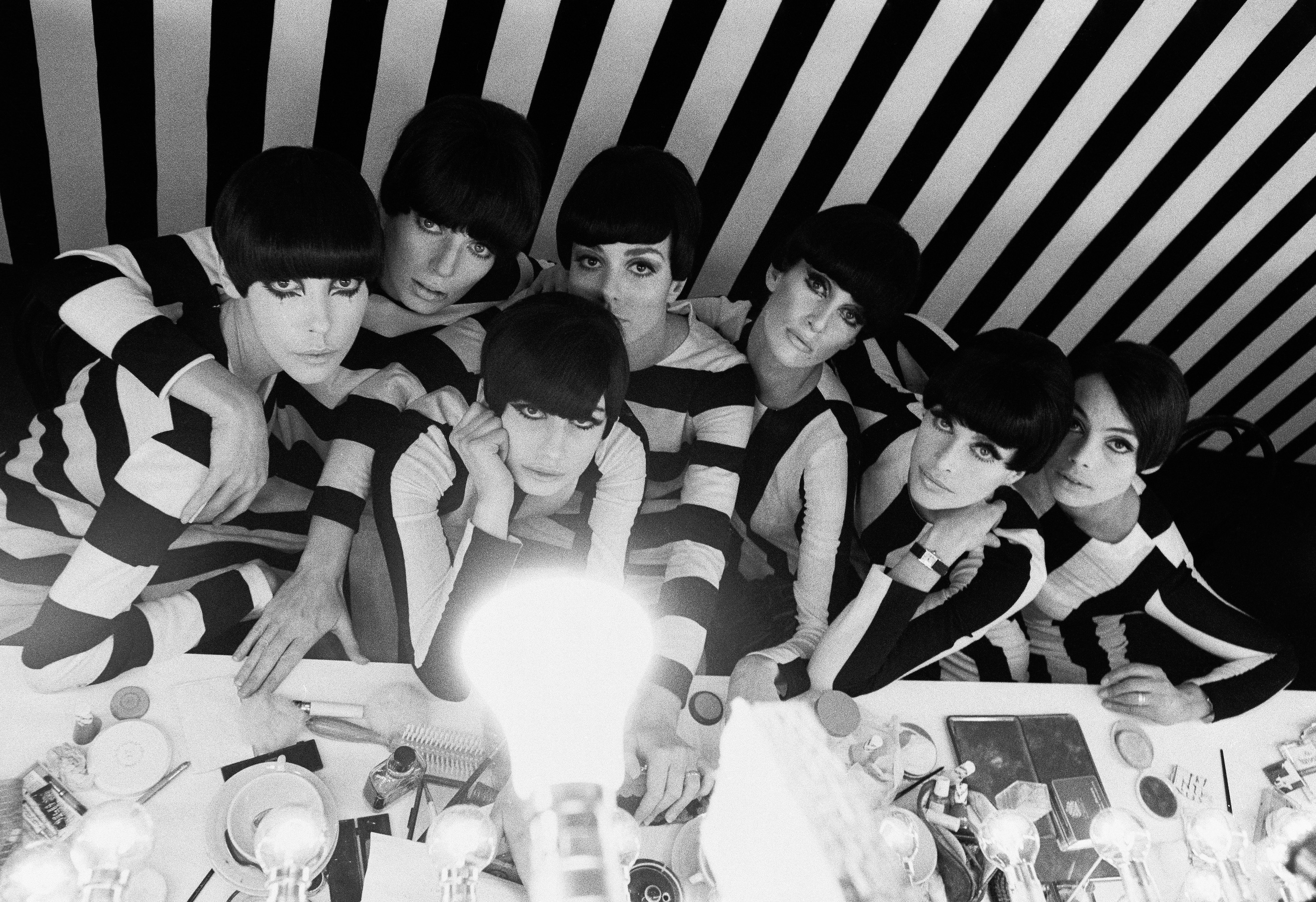 Black-and-white photo of models in striped tops posing at a makeup table
