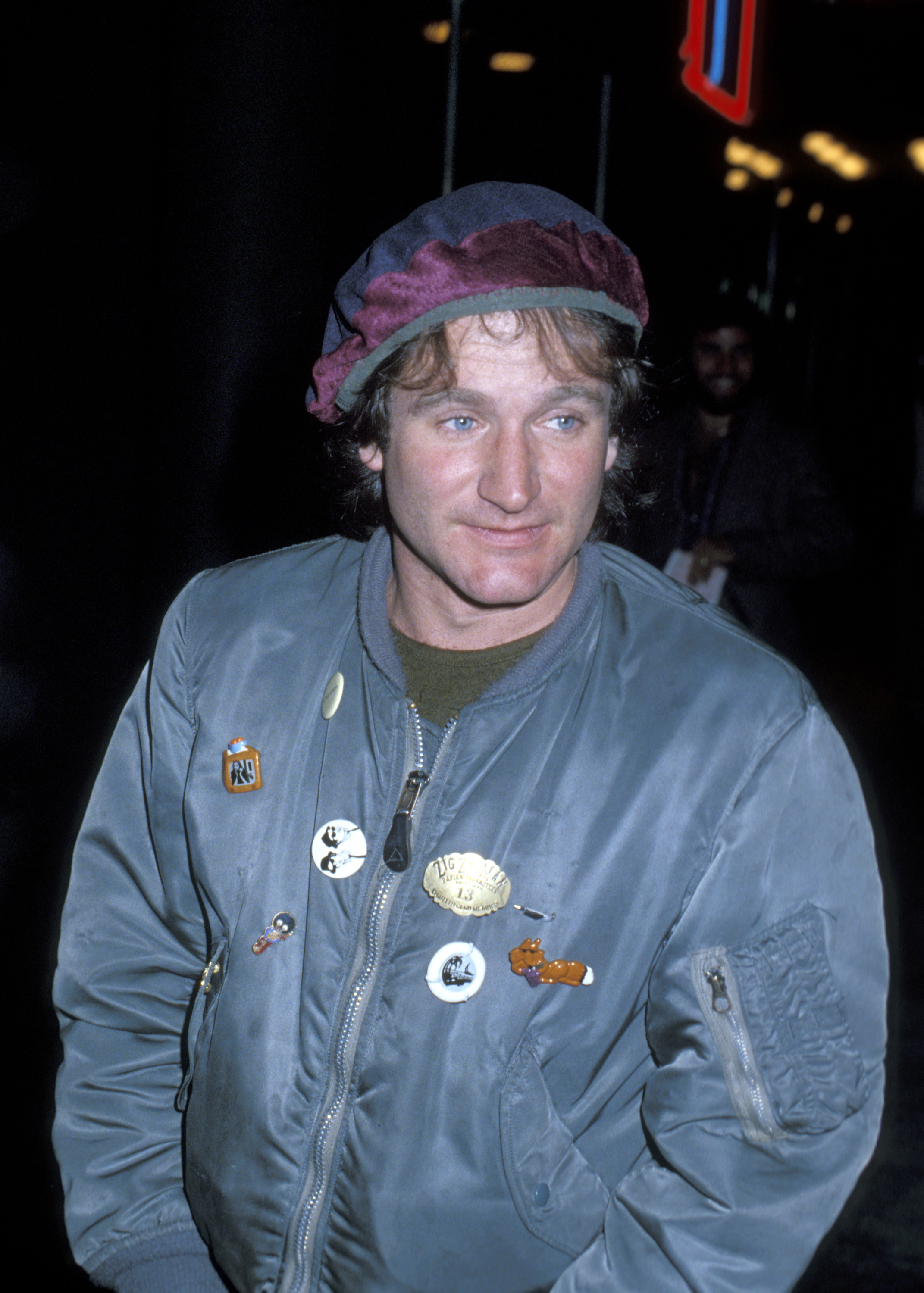 Robin Williams in a blue and purple beret and a blue bomber jacket with pins on it at the Roxy in 1979