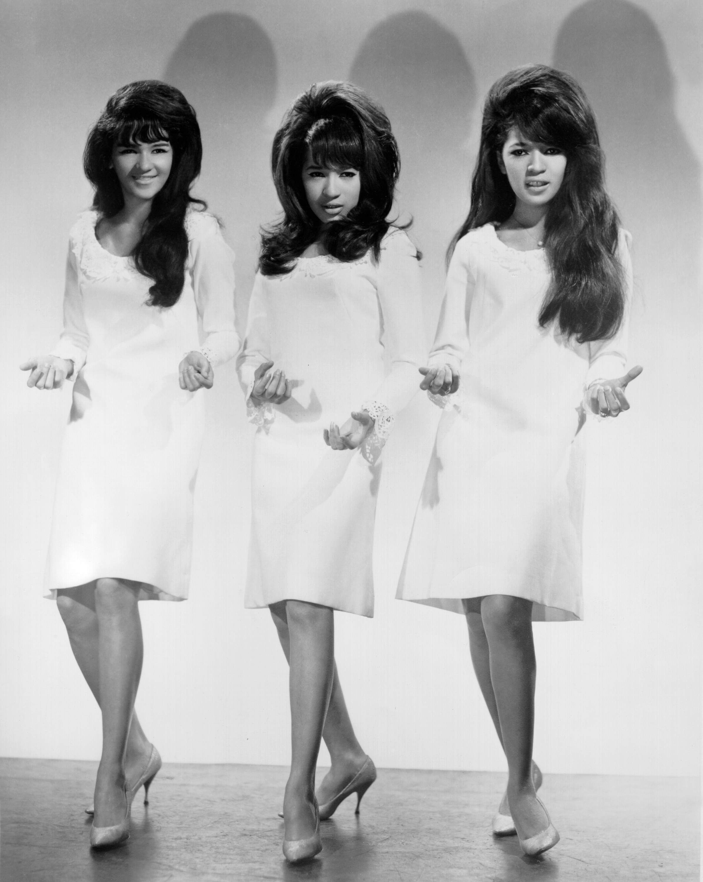 the ronnettes posing in white mod dresses, bouffant hair and cat eye eyeliner performing in 1964