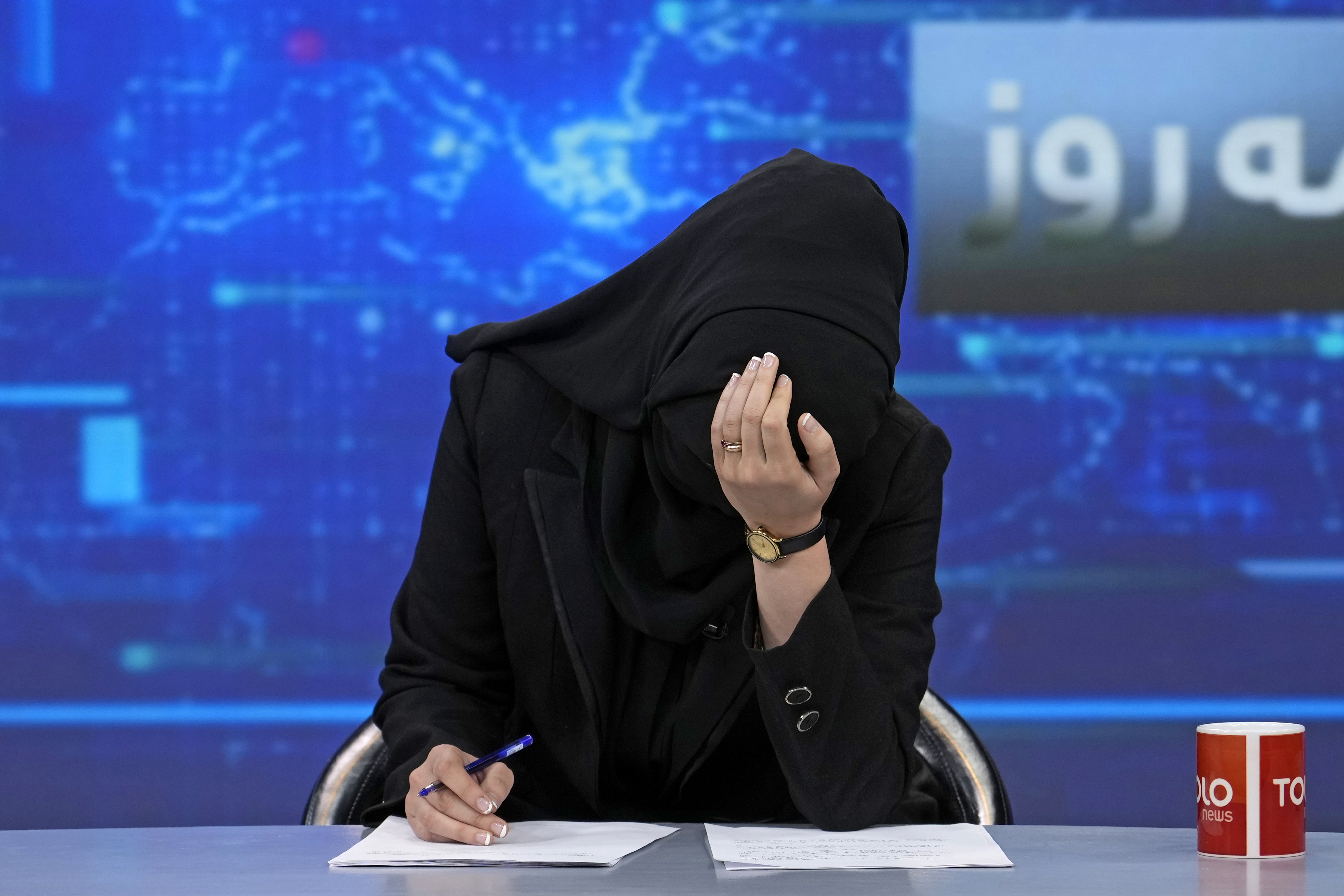 Perempuan berpakaian serba hitam menundukkan kepala saat membacakan berita