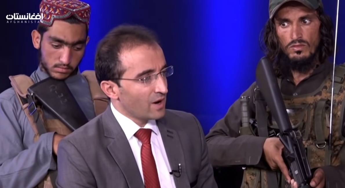 Dua serdadu Taliban membawa senjata berdiri di belakang seorang laki-laki