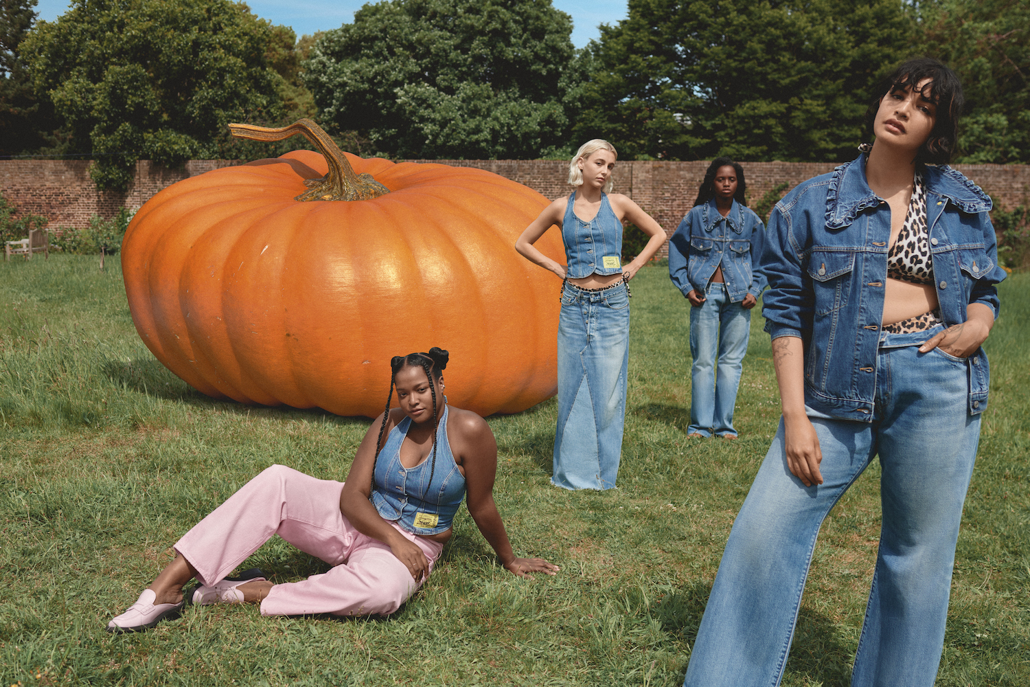 Emma Chamberlain and three other models wearing denim looks next to a giant pumpkin