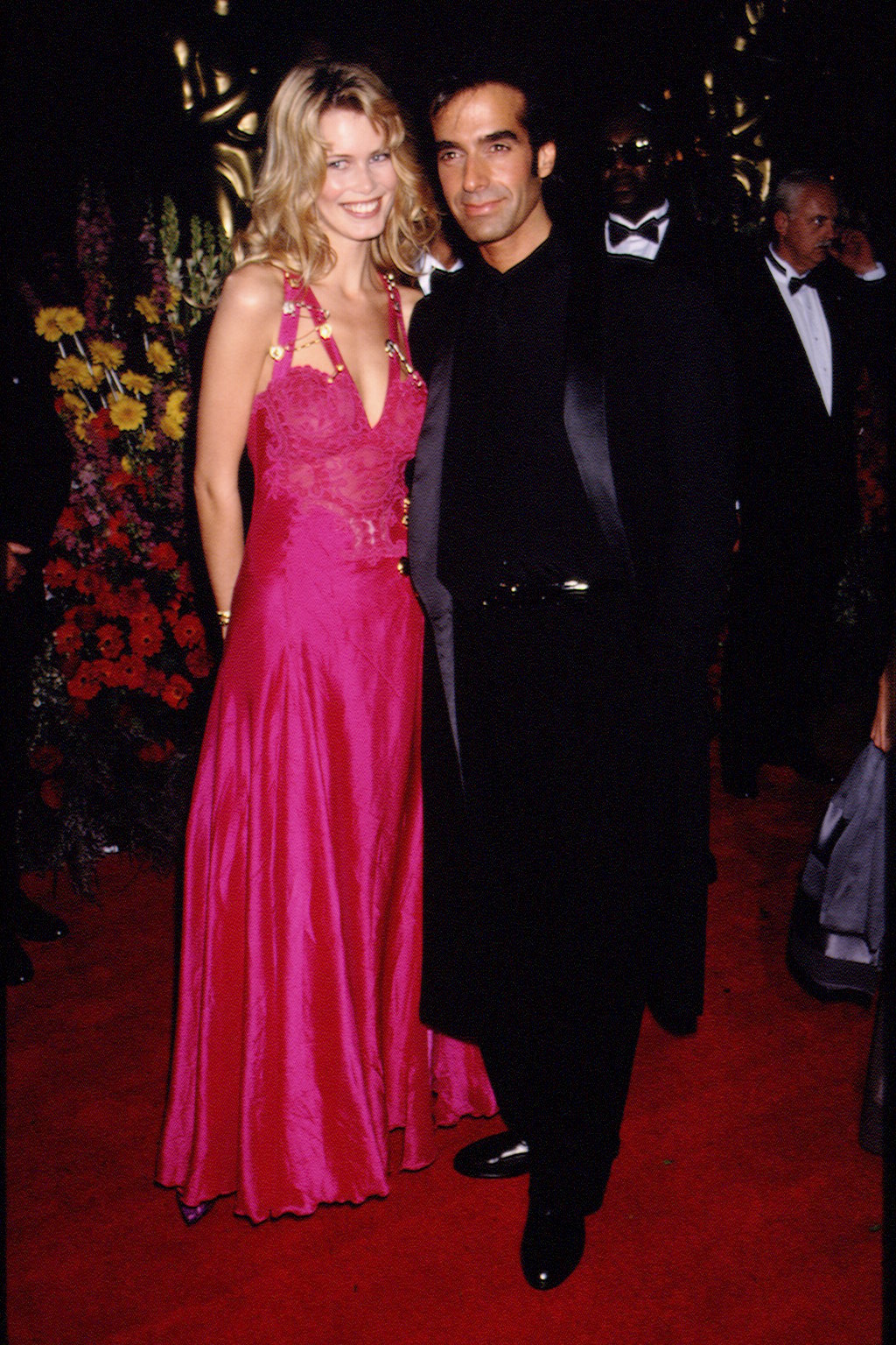 claudia schiffer posing in a hot pink versace safety pin dress with david copperfield on the red carpet 1994