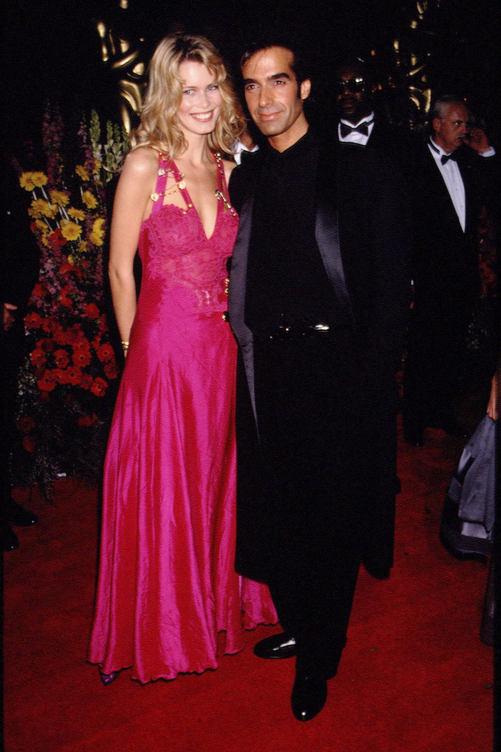 Claudia Schiffer poses in a pink safety pink Versace dress with David Copperfield on the red carpet in 1994