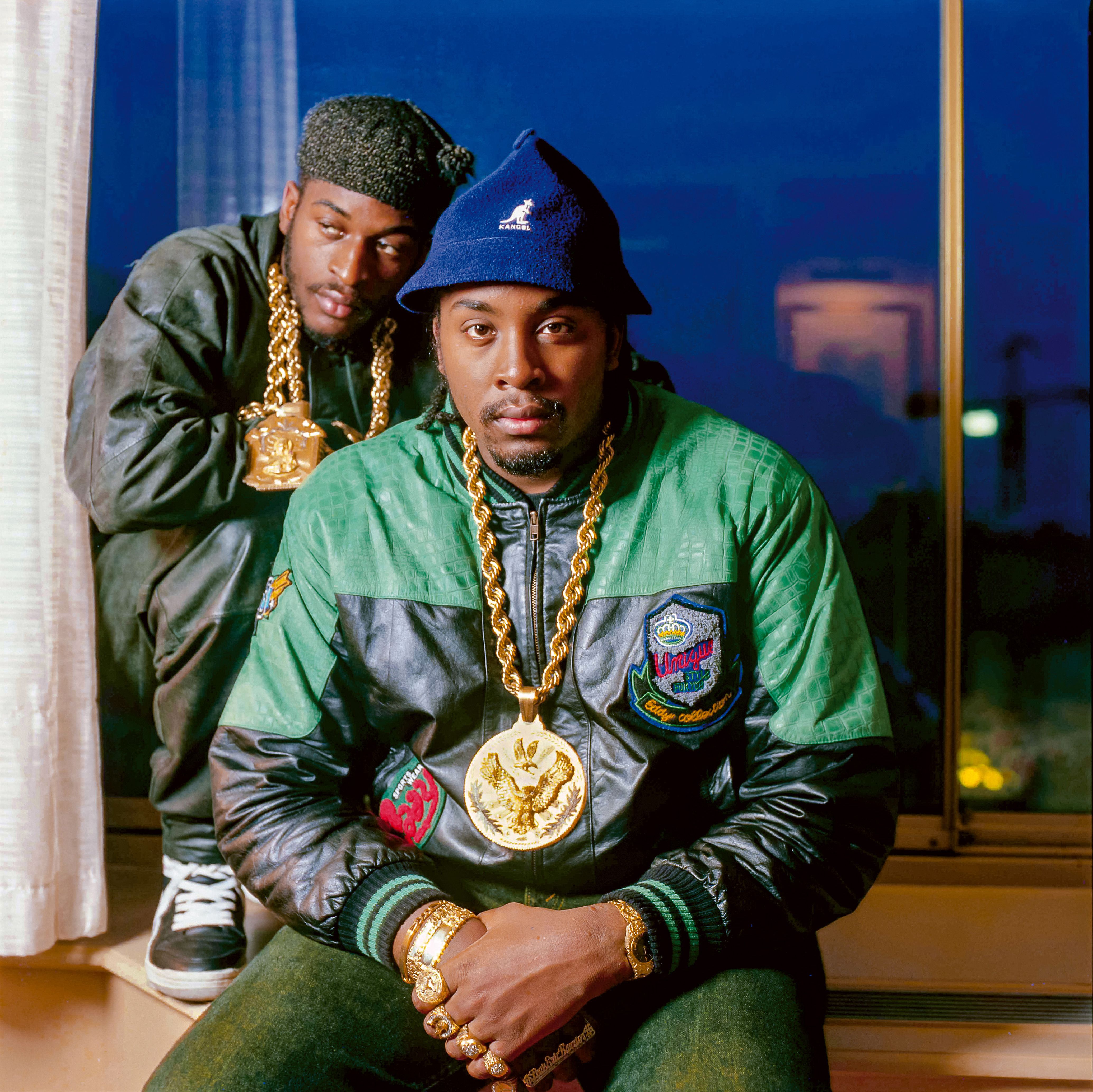 Rakim wears a Mary pendant on layered gold rope chains, while Eric B. wears an anchor pendant and eagle motif pendant on gold rope chain, gold nugget watch, and multiple gold nugget rings, including pinky ring with a Mercedes-Benz motif and a fourfinger nameplate ring spelling out his full name— Louis Eric Barrier— in classic script