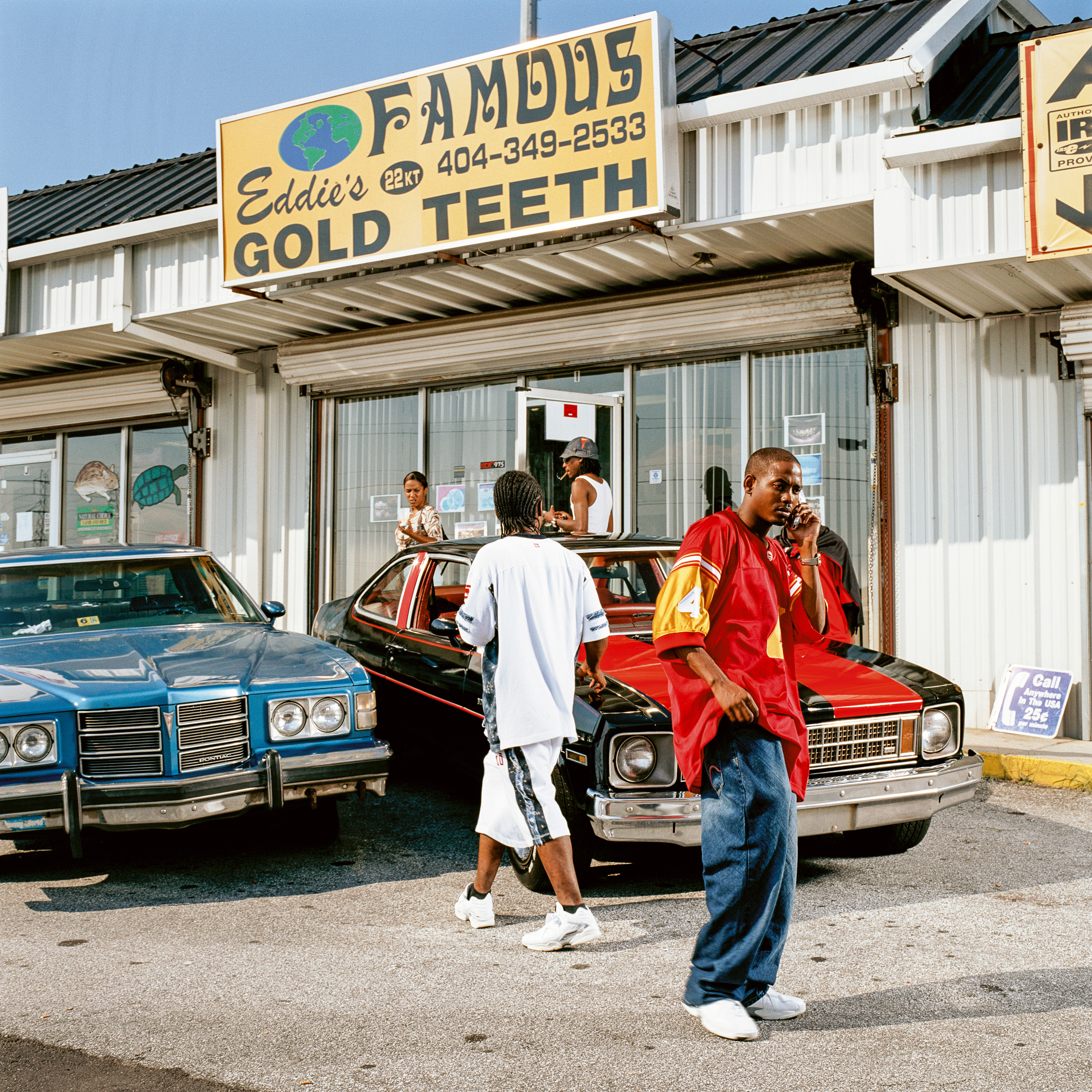 Ein Foto eines Juweliers in Atlanta. Vor dem Laden stehen zwei Autos. Davor und dahinter laufen mehrere Schwarze Männer und Frauen. Ein Mann trägt ein rotes Shirt, Baggy Pants und telefoniert