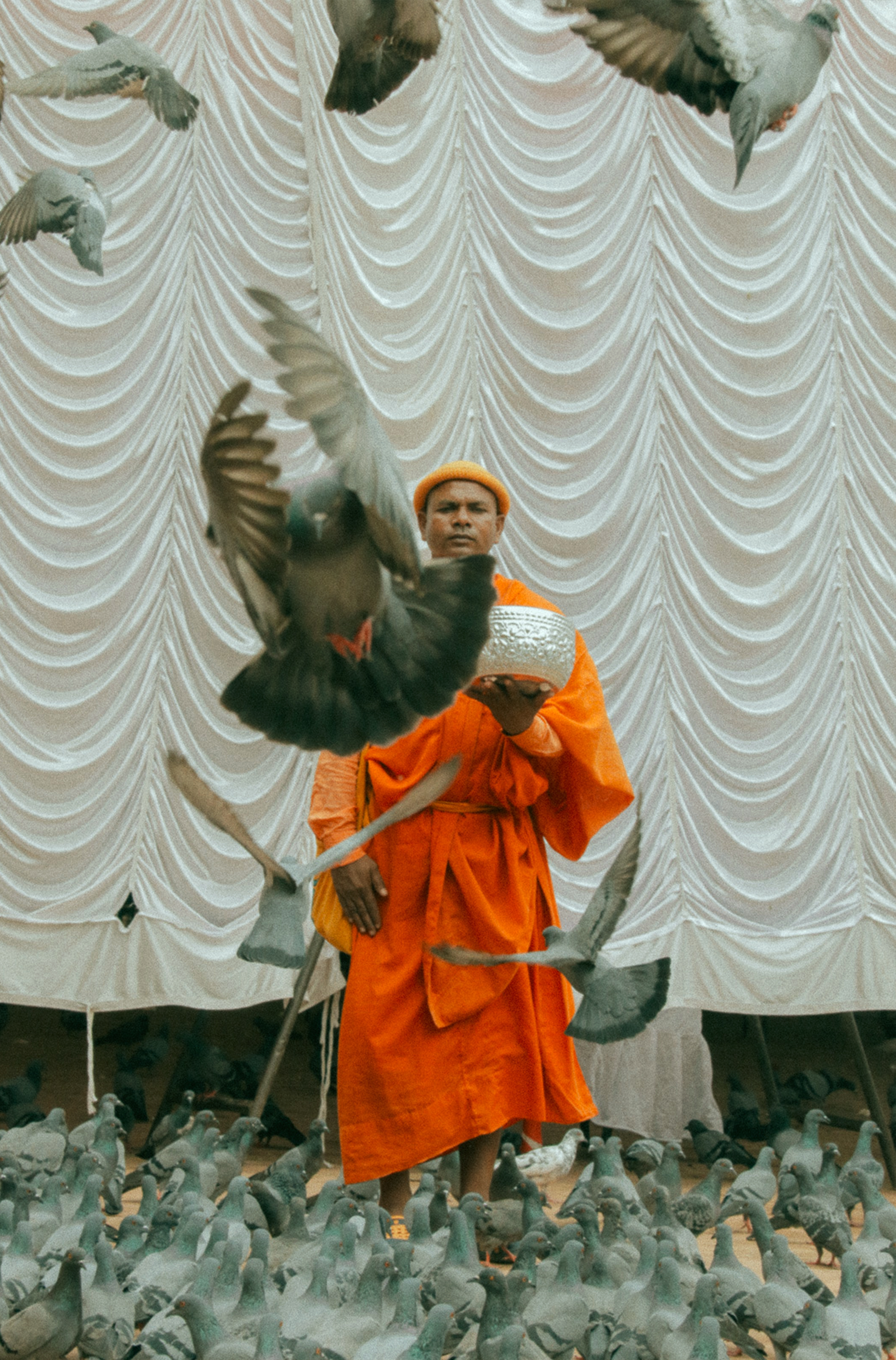 Lelaki mengenakan jubah biksu oranye berdiri di depan gorden putih