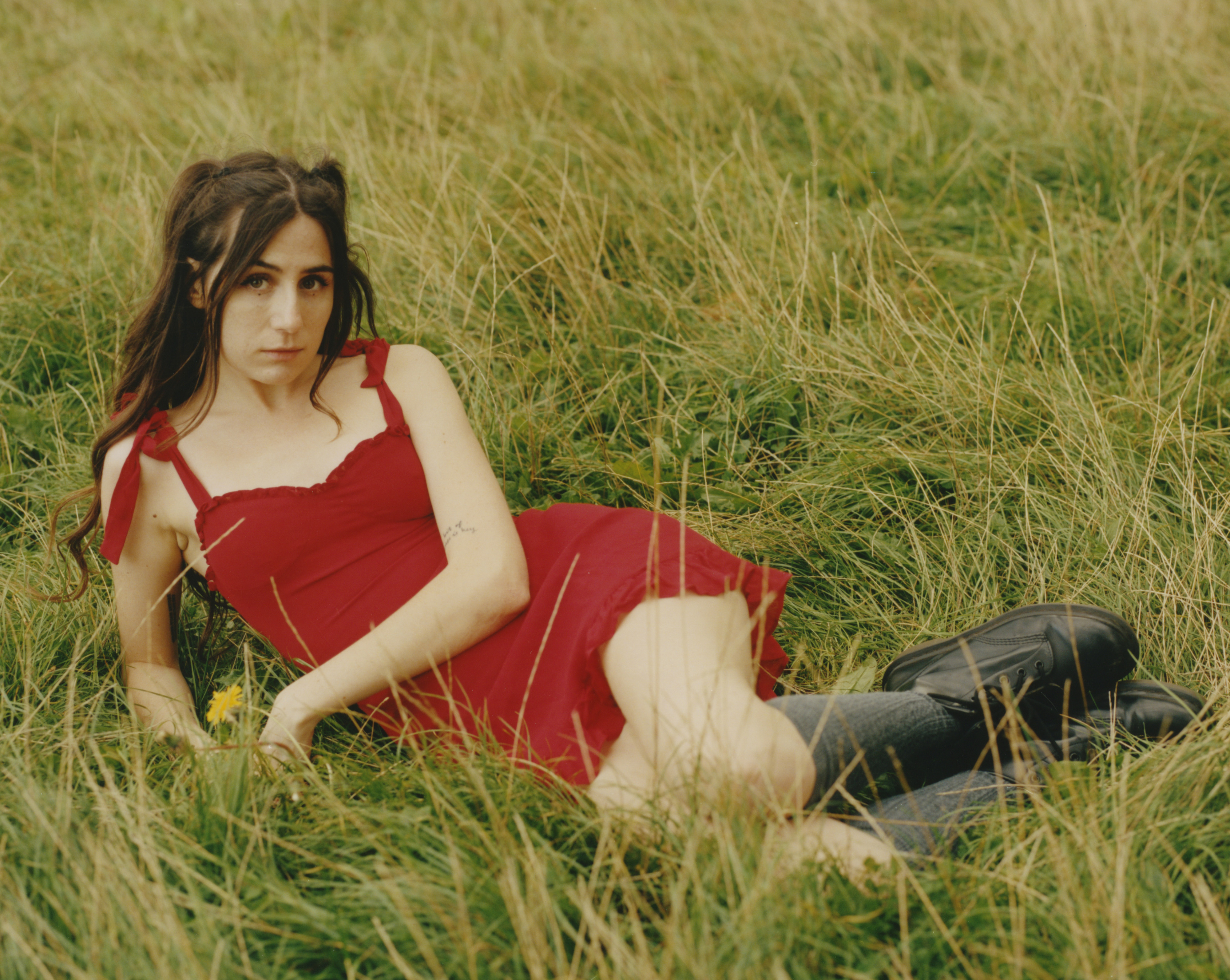 dodie lying in a field of grass, wearing a bright red dress