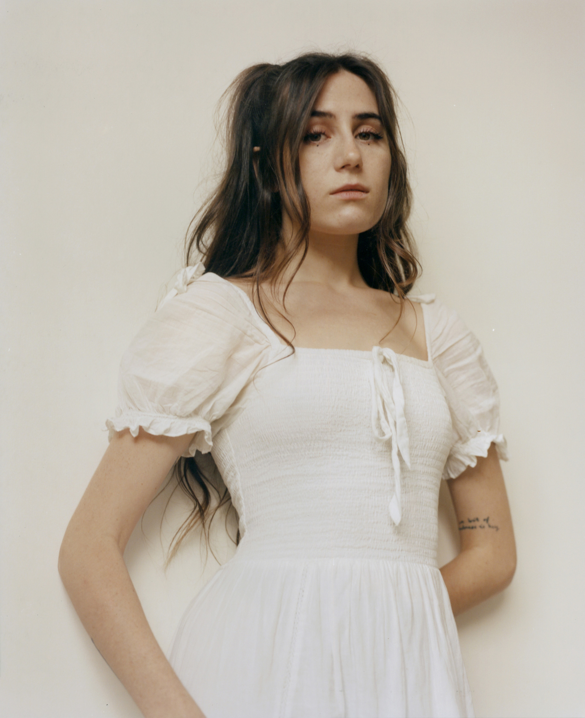 a portrait of dodie in a white dress standing against an off white background