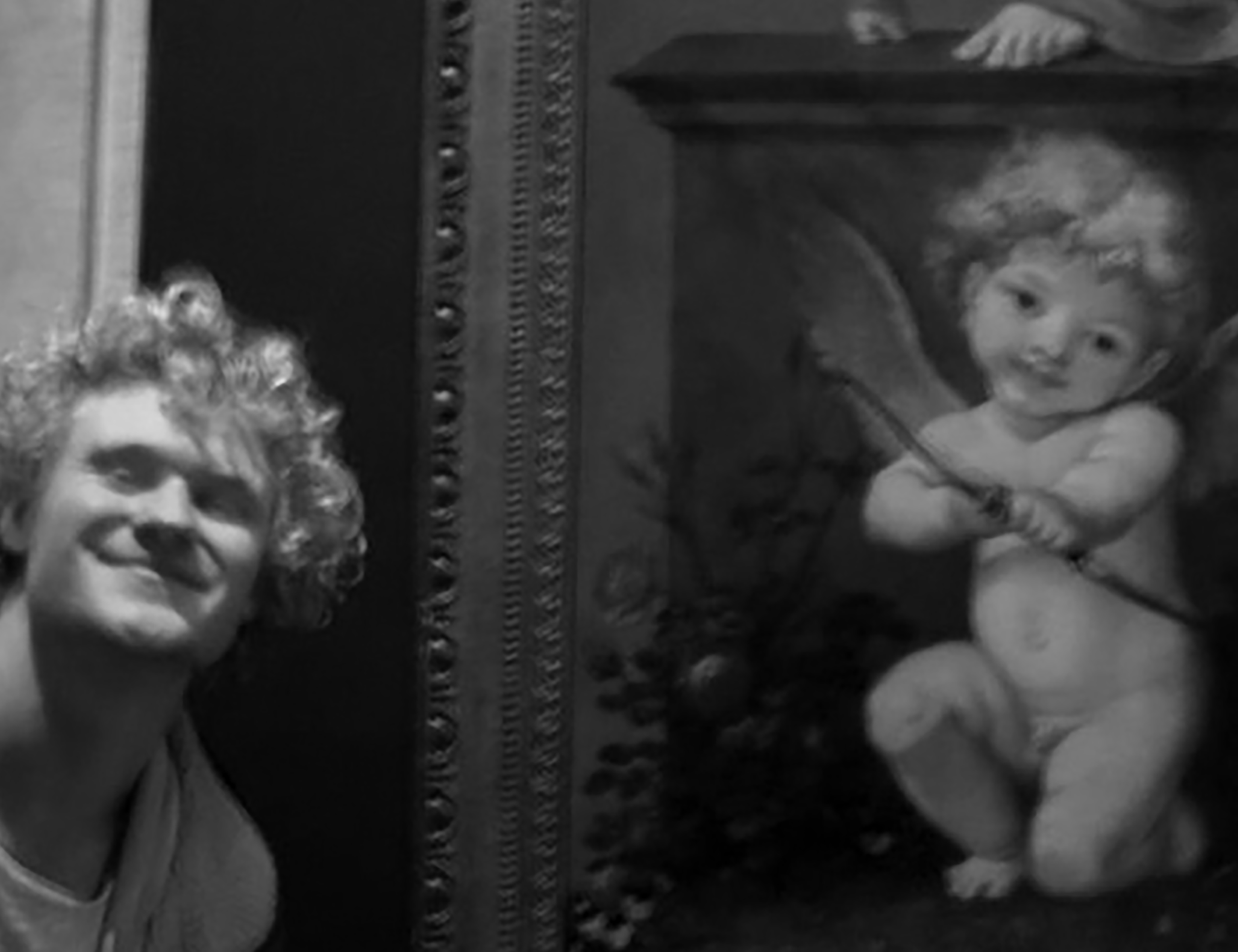 Laki-laki berambut ikal berpose di depan lukisan dewa cinta berambut ikal